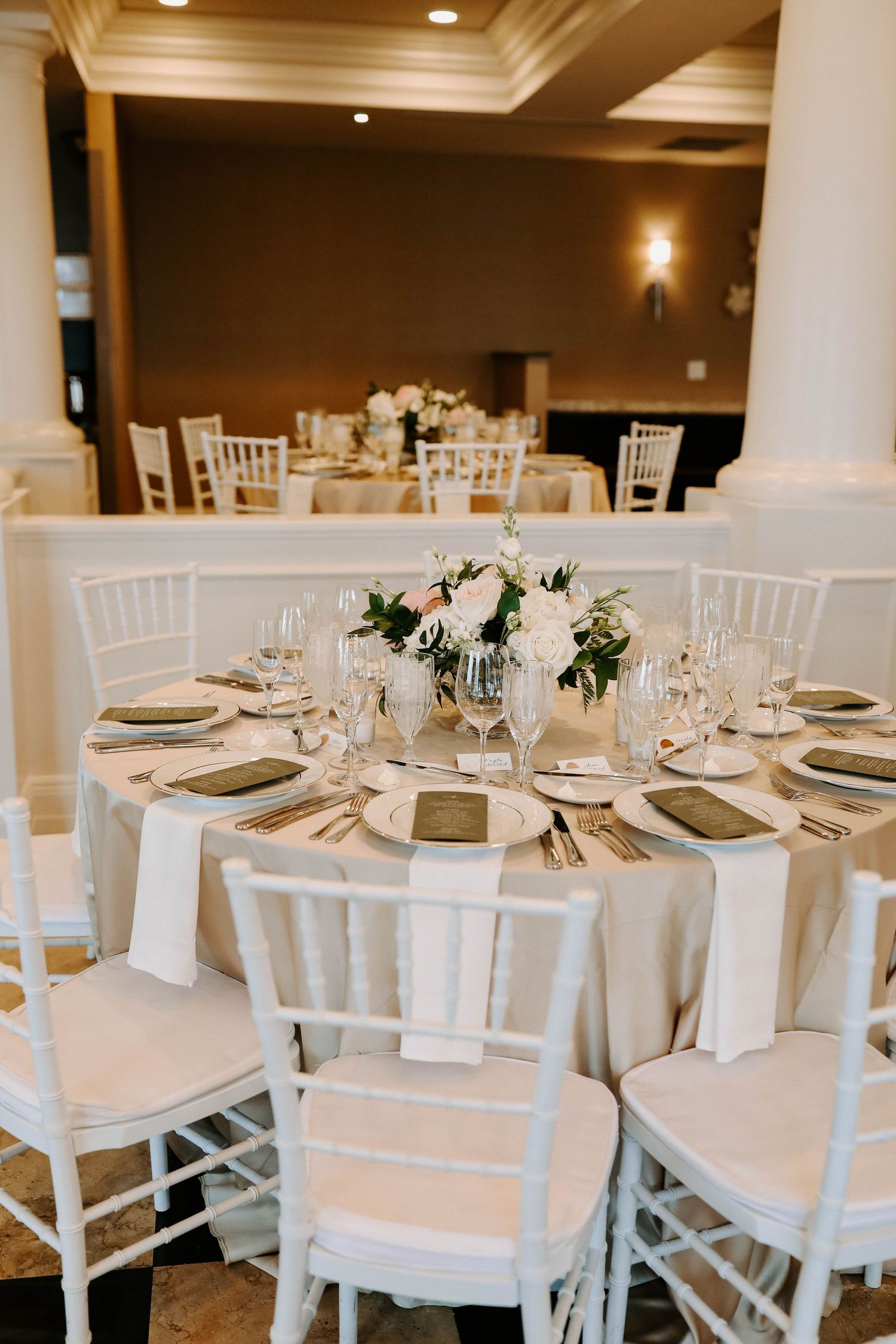 A formal wedding table setting with white chiavari chairs and delicate floral arrangements.