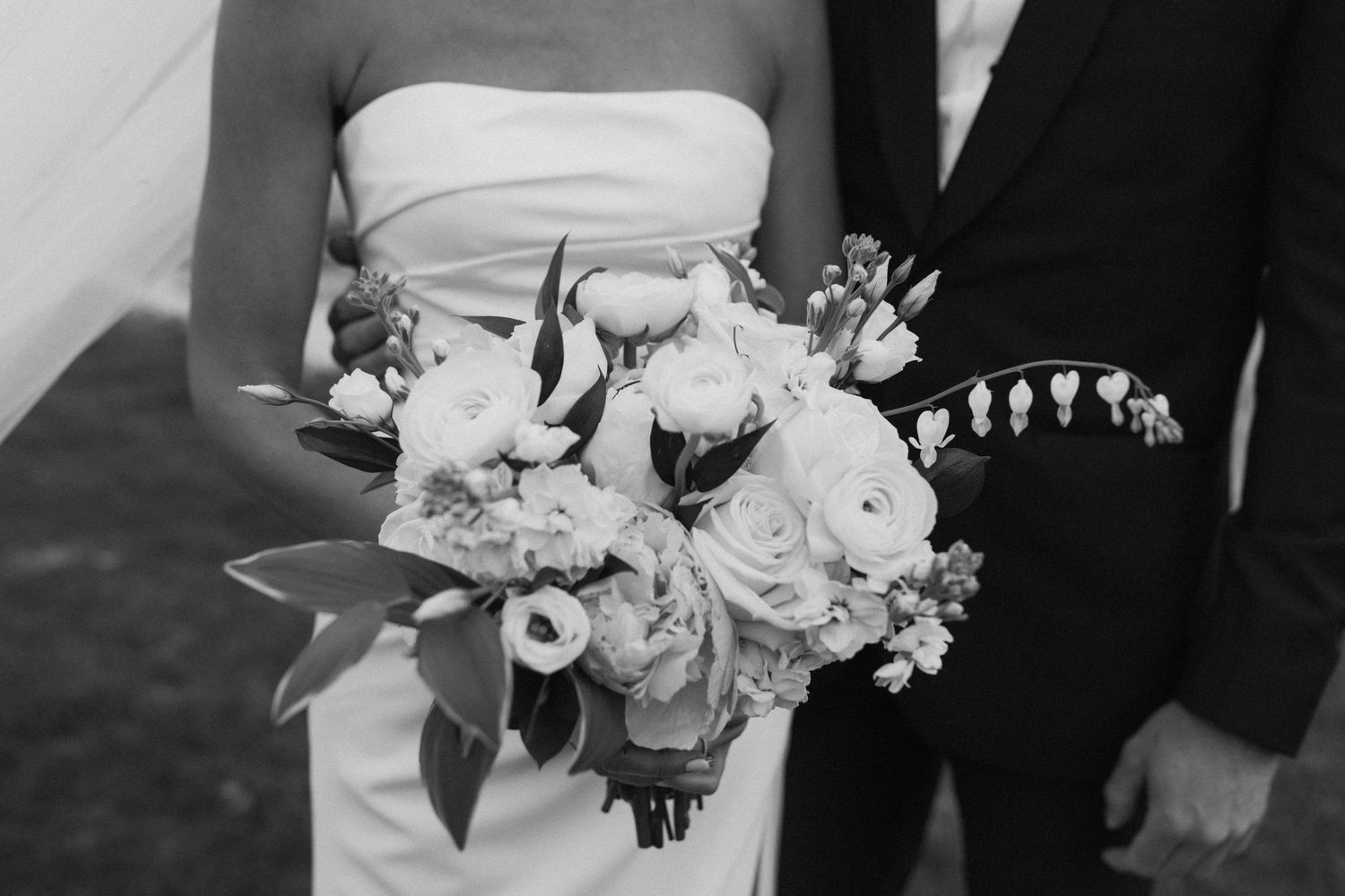 Elegant white wedding bouquet with roses and delicate greenery against a black suit.