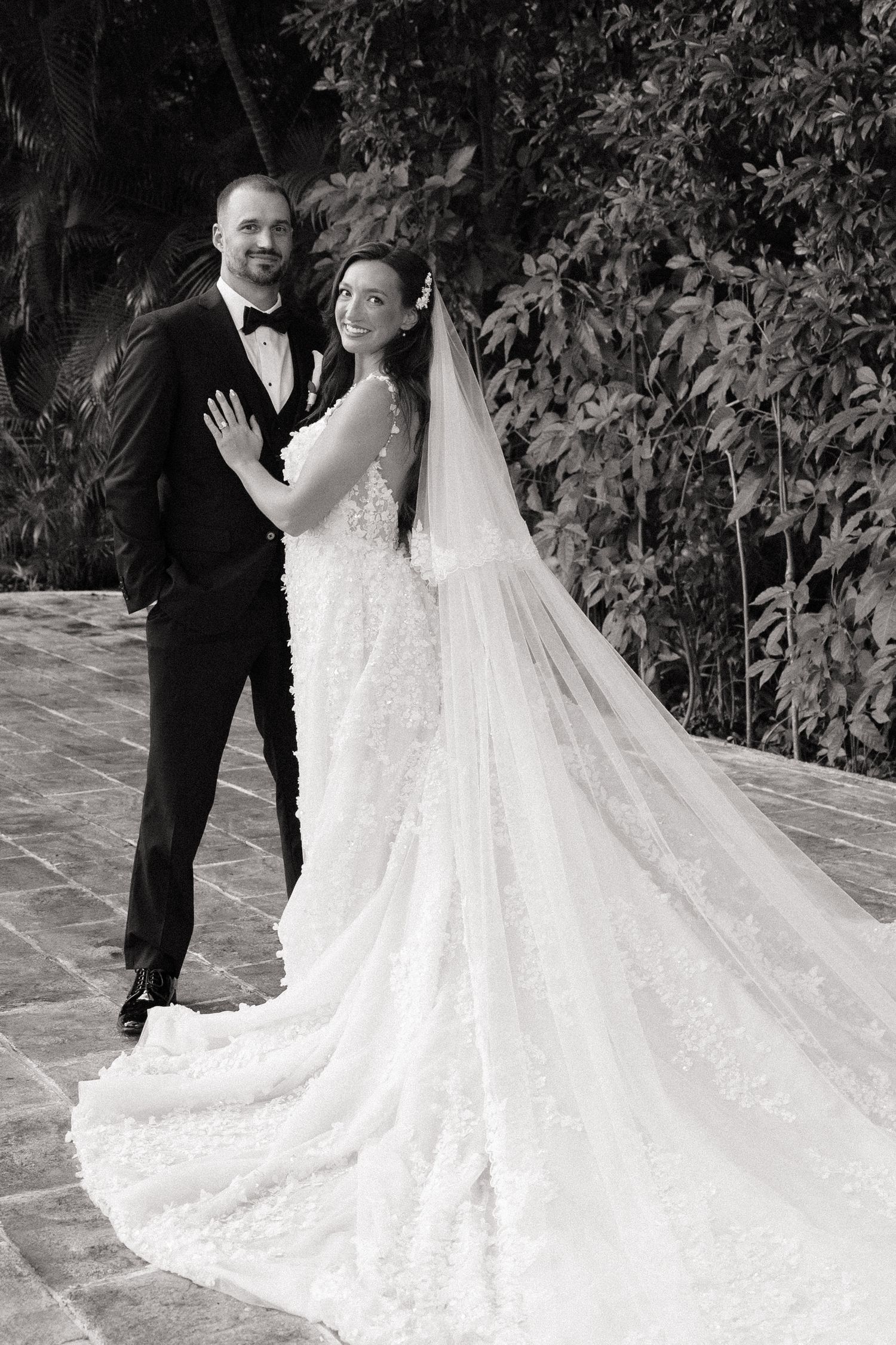 Black and white photo of wedding couple with dramatic train on stone terrace.