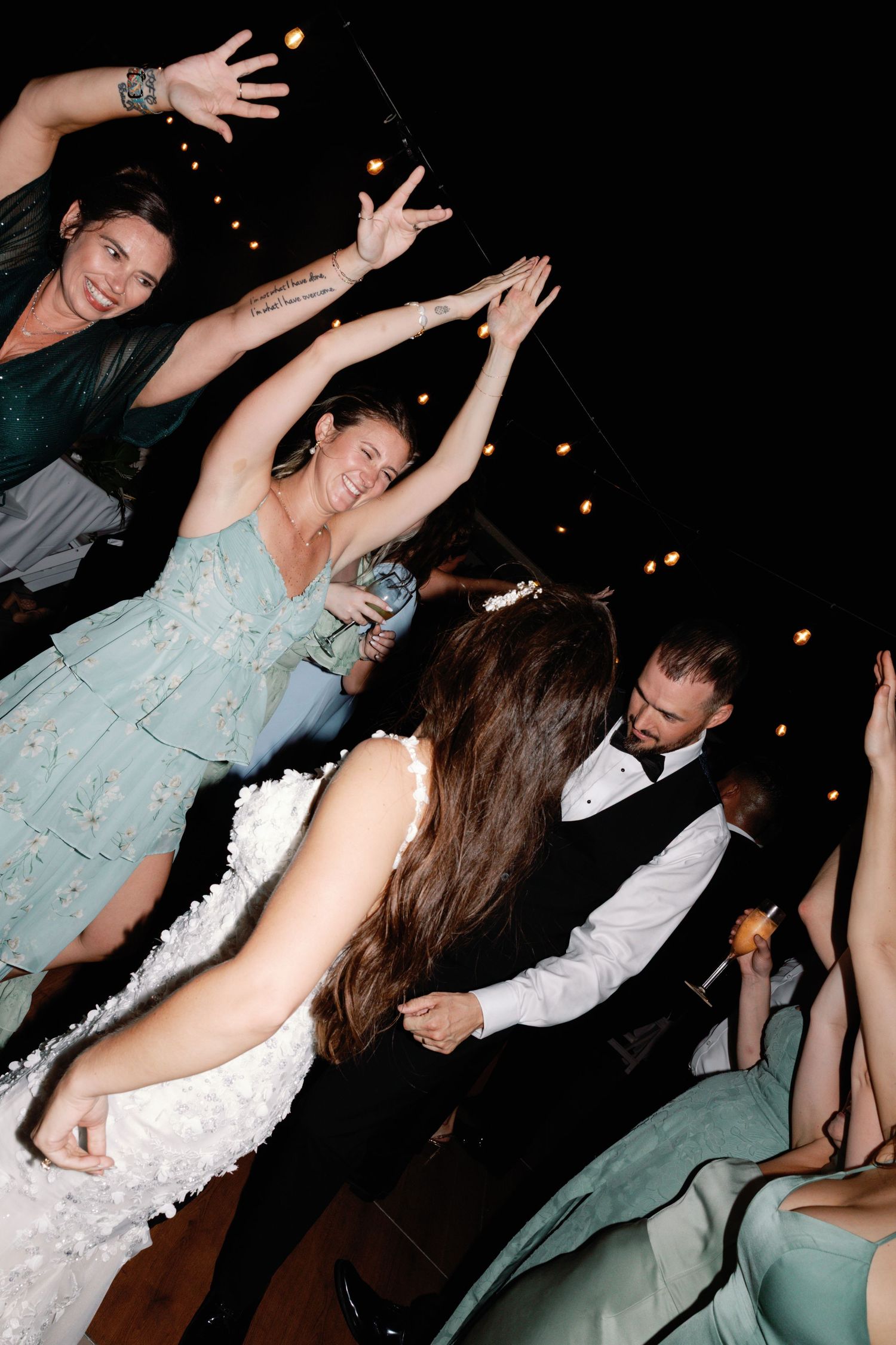 Wedding party members dance energetically in mint green dresses and formal attire.