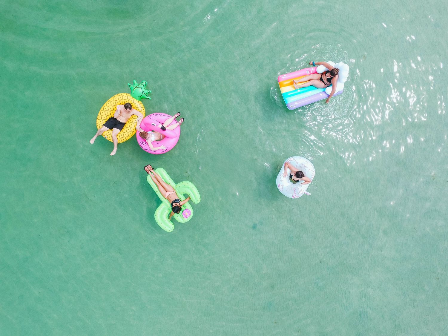 Colorful inflatable pool floats and toys drift on turquoise water creating a playful summer scene.