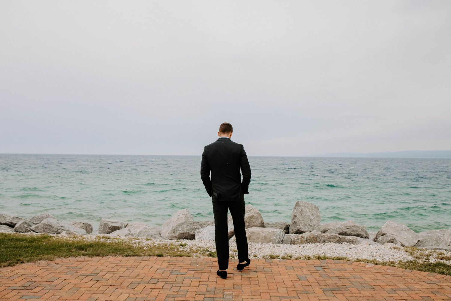 A lone figure stands on a brick pathway overlooking a serene ocean view.