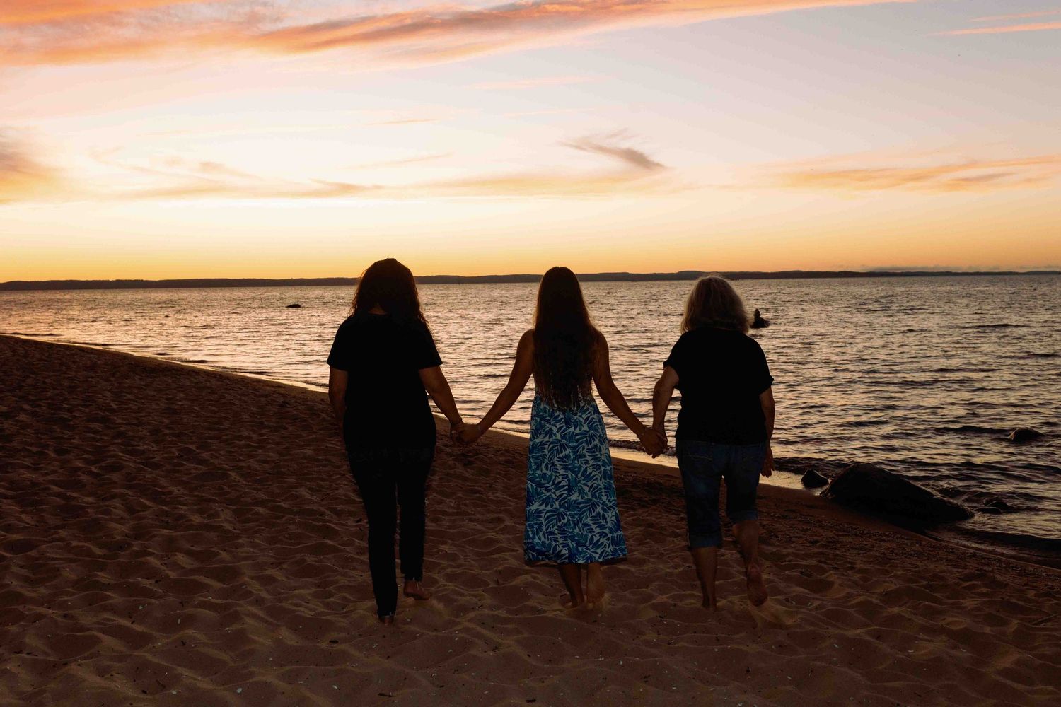 Dark silhouettes against an orange sunset sky on a beach.