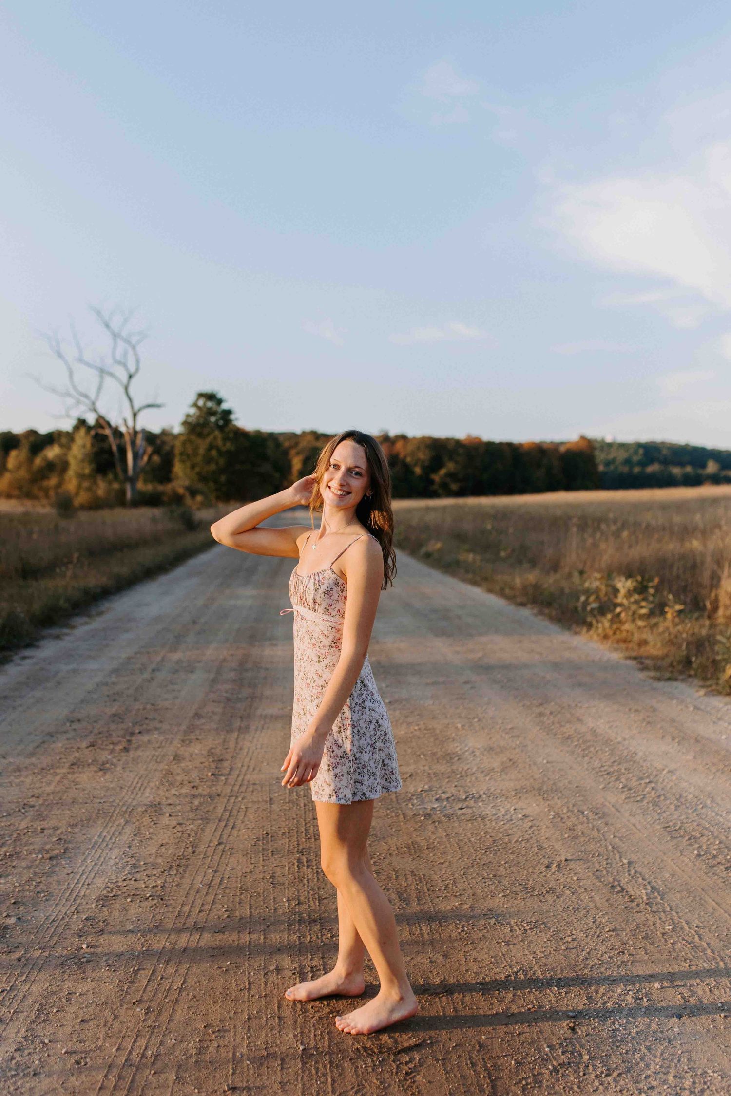 A person dances freely on a rural dirt road with autumn trees in the distance.