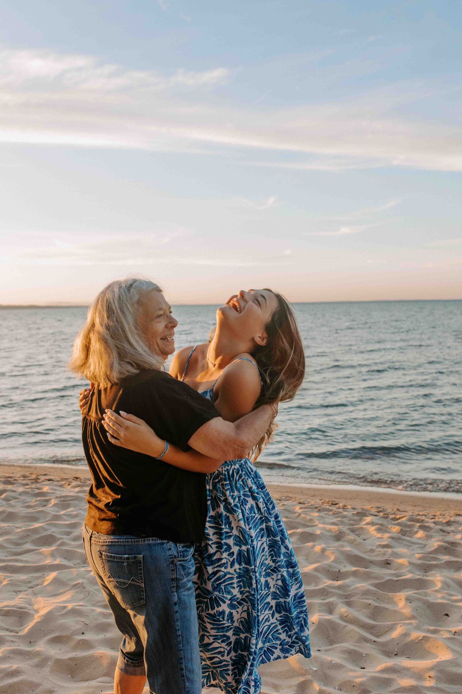 Two people share an energetic moment together on a beach with waves and sunset in the background.