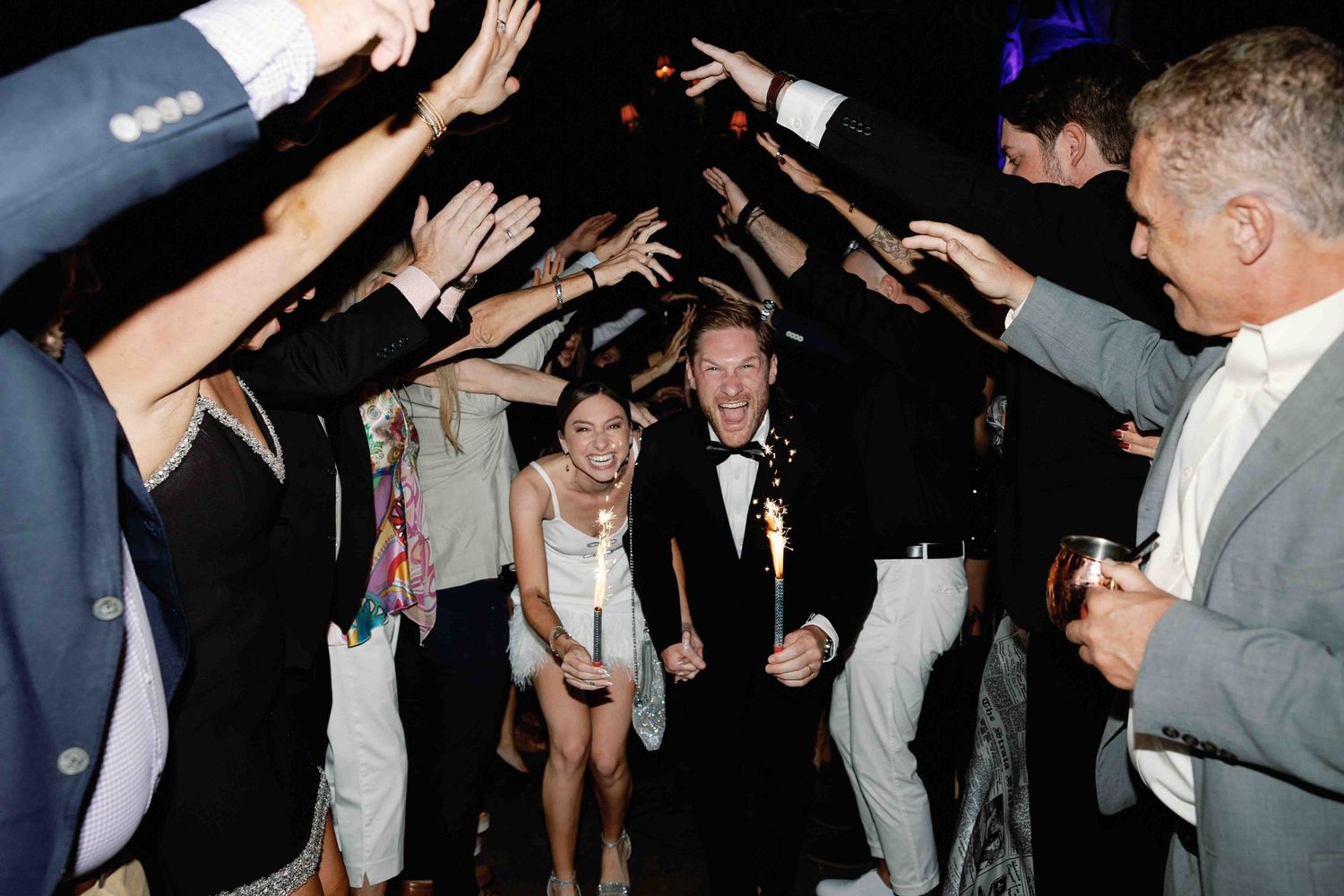 Wedding reception guests dance and celebrate on a dark dance floor.