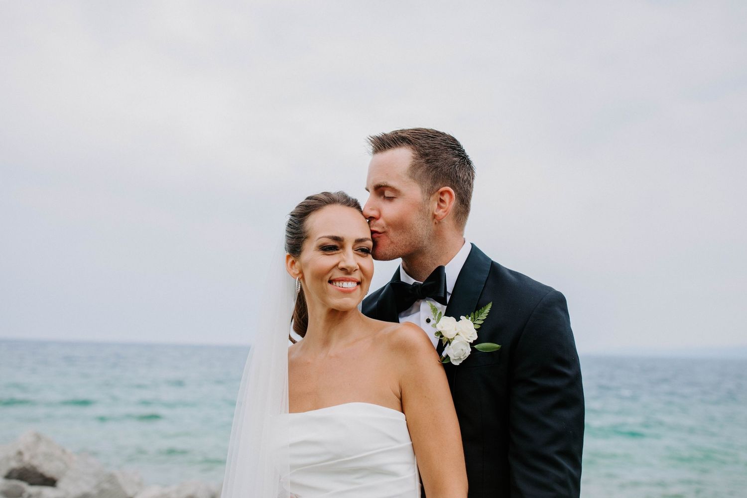 A joyful wedding couple sharing an intimate moment by the ocean with turquoise waters in the background.