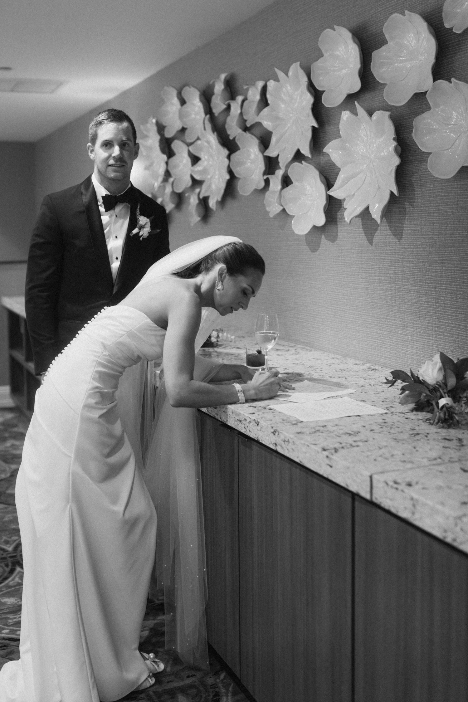 A person in a white dress signs a document at a reception desk decorated with white paper butterflies.