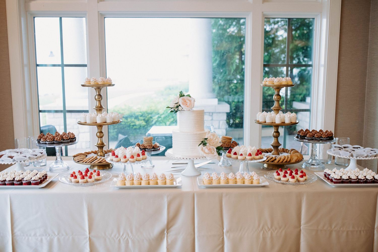 A white dessert table featuring a wedding cake, cupcakes and various sweet treats.