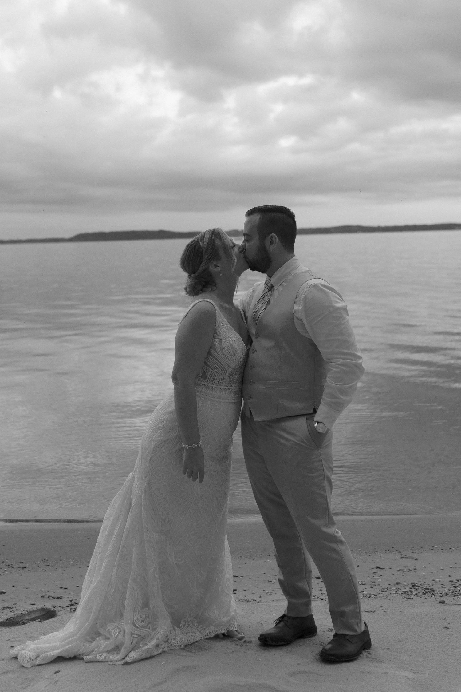 A black and white beach portrait of a couple in wedding attire.