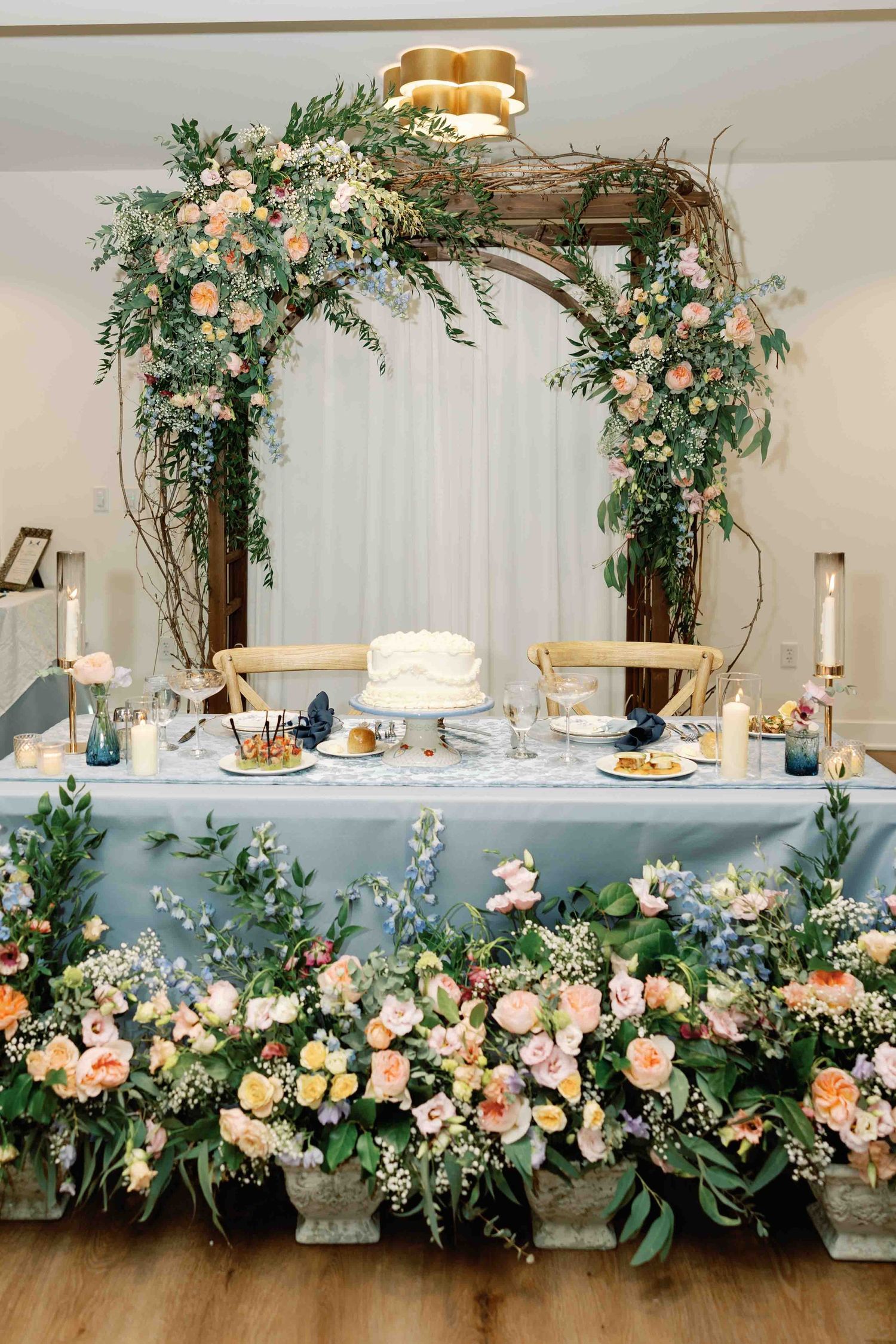 Luxurious floral arrangements with peach roses and greenery decorating a white wedding reception table.
