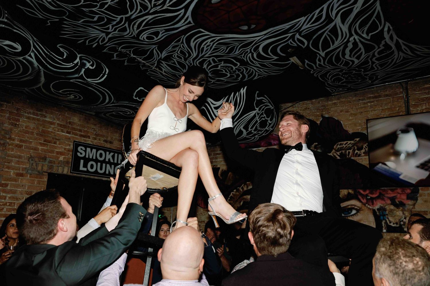 Energetic dancing and celebration inside a brick-walled venue with lounge signage.