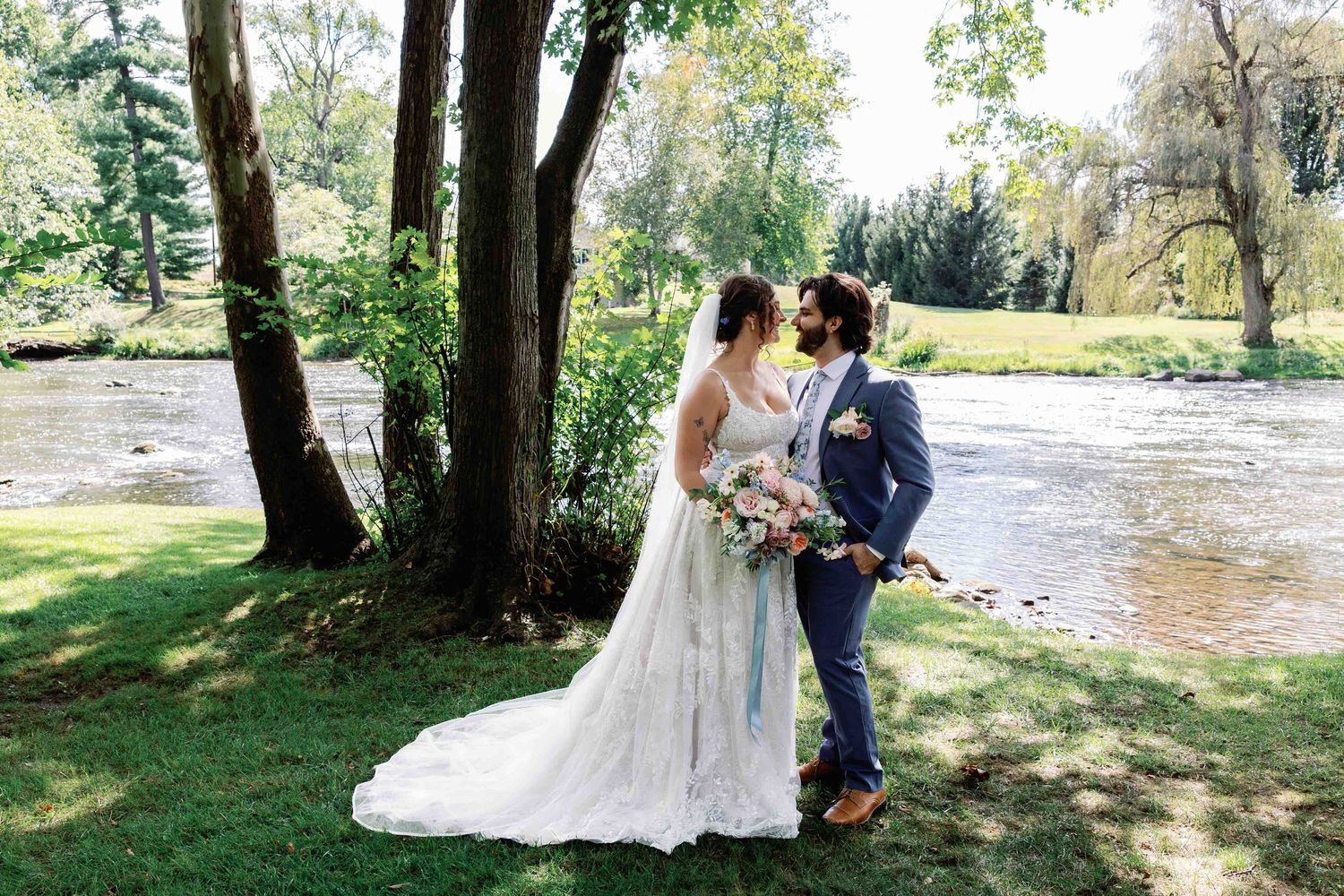 A wedding couple poses together in a natural outdoor setting with trees and a river in the background.