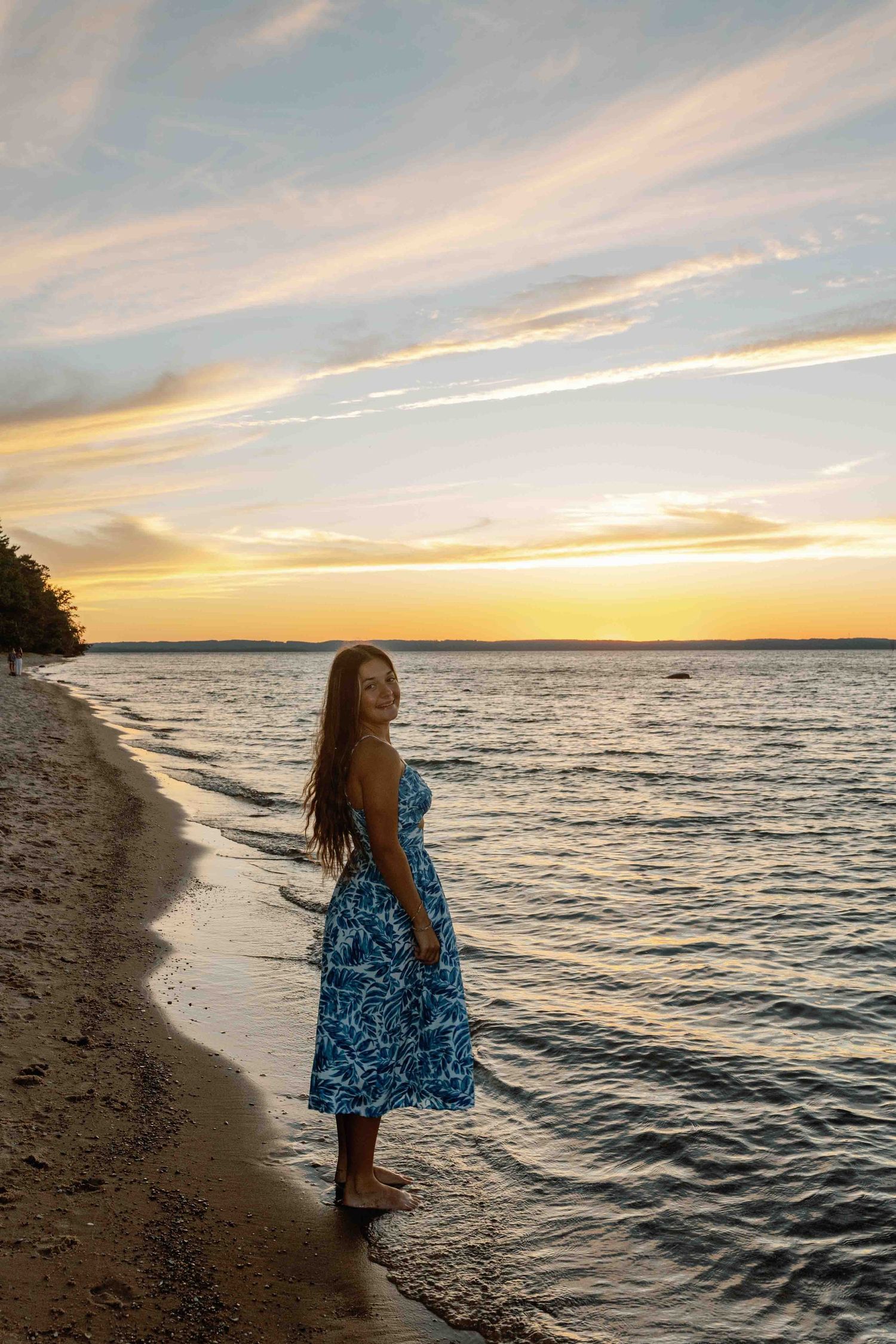 Silhouette against a golden sunset stands on a peaceful beach wearing a flowing blue dress.