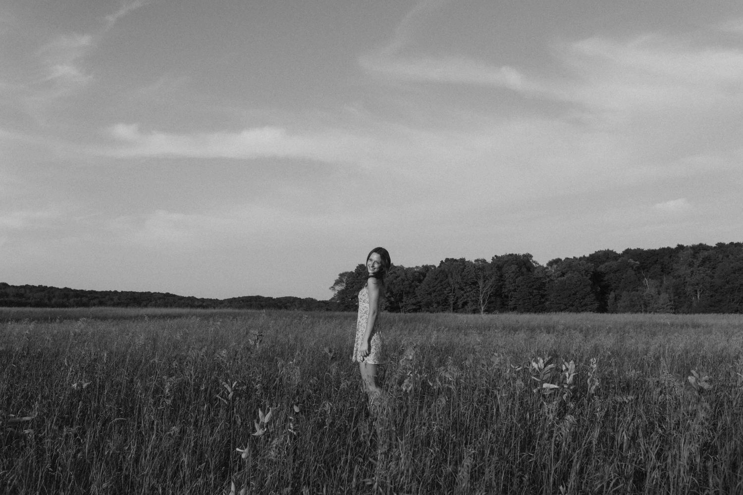 Black and white panoramic view of a person in a field with trees on the horizon.