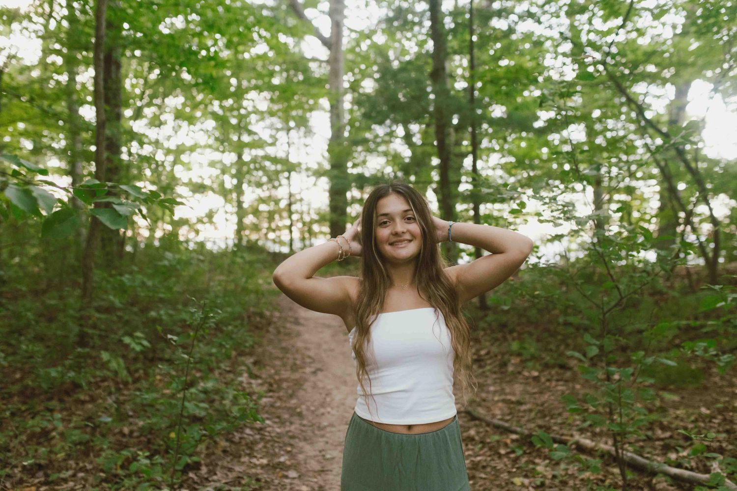A wooded nature trail winds through lush green forest with dappled sunlight filtering through the trees.