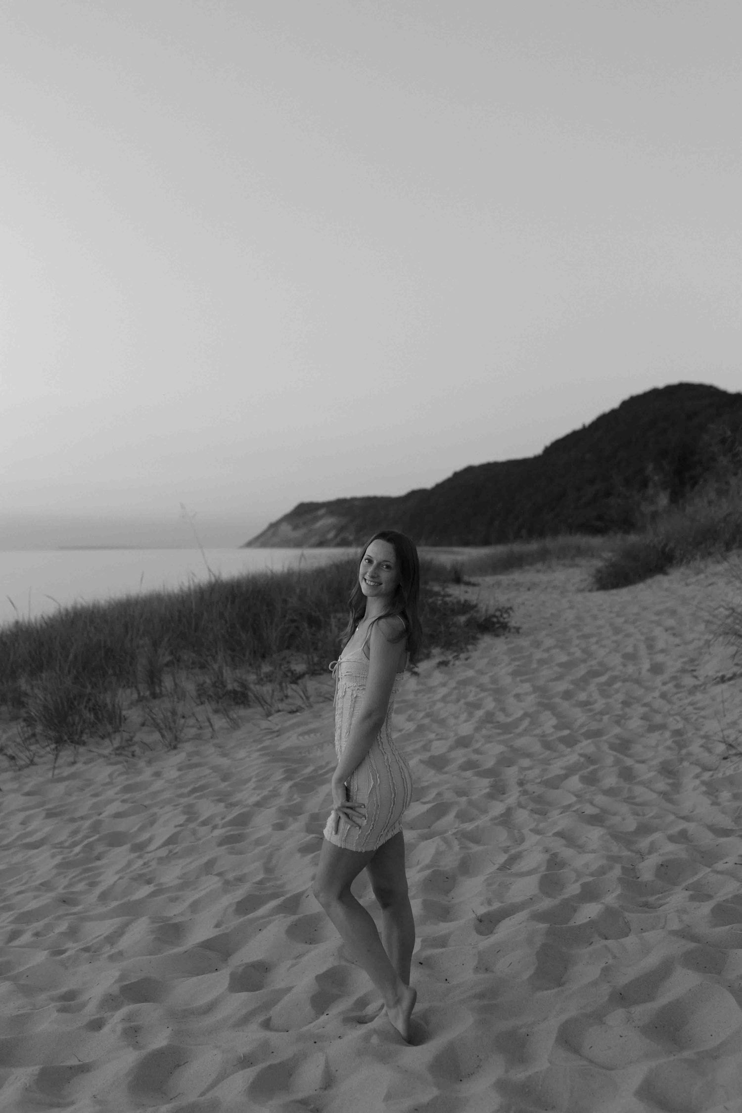 Figure walks along sandy beach dunes in dramatic black and white lighting.