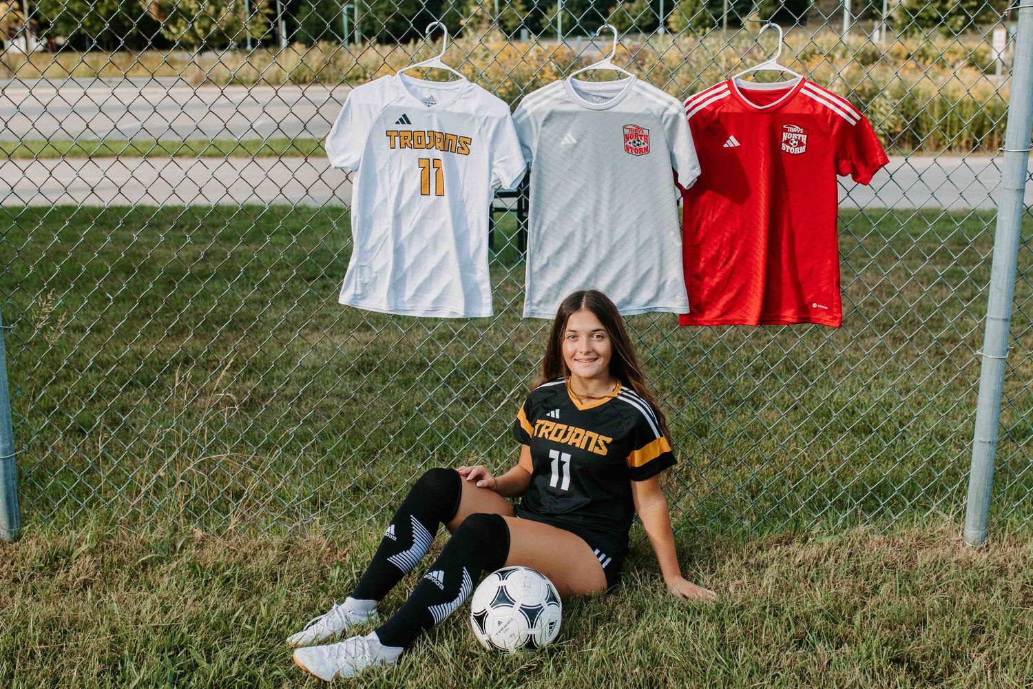 White and red soccer jerseys displayed on chain link fence.