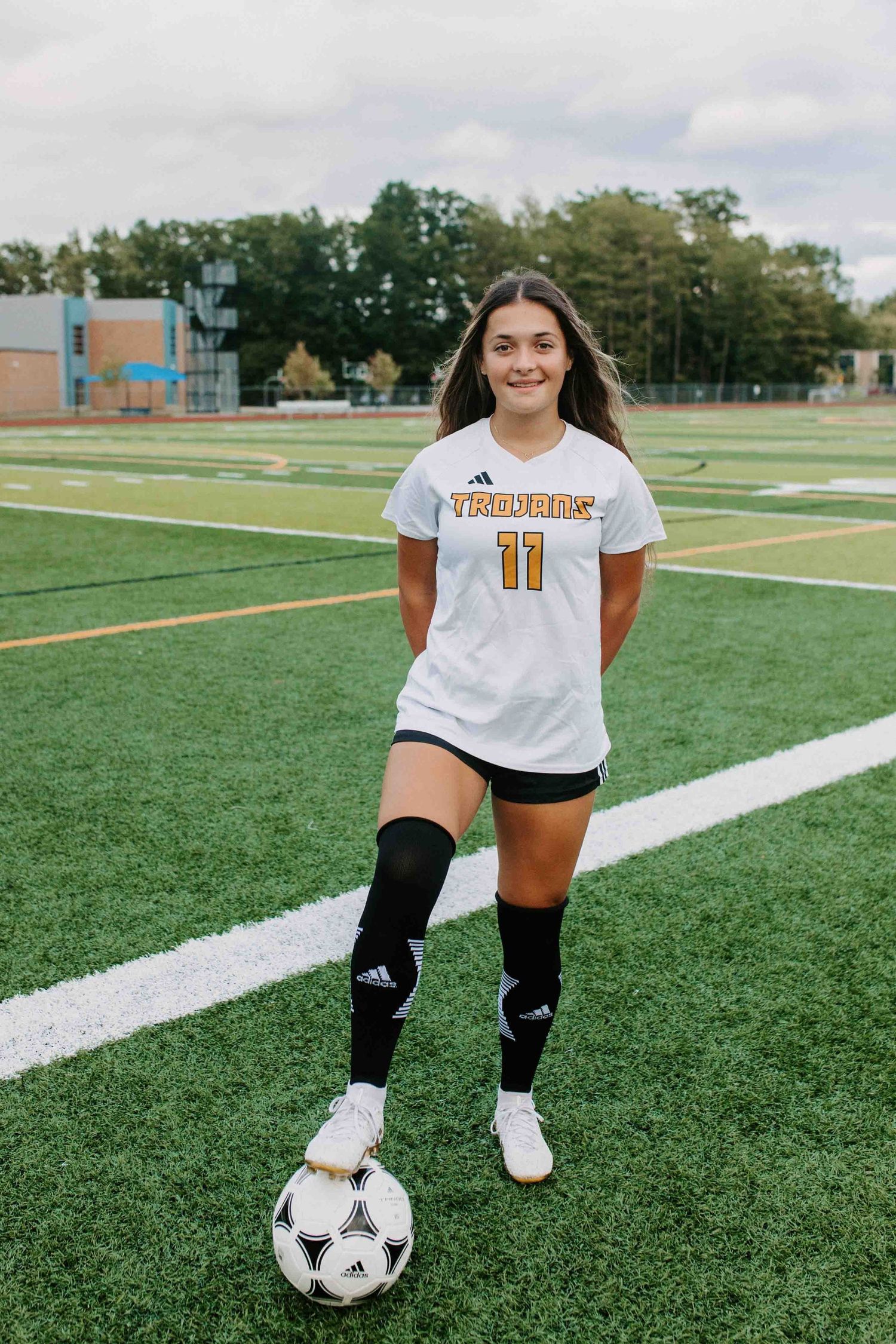 Soccer player in white uniform kneeling with ball on green turf field.