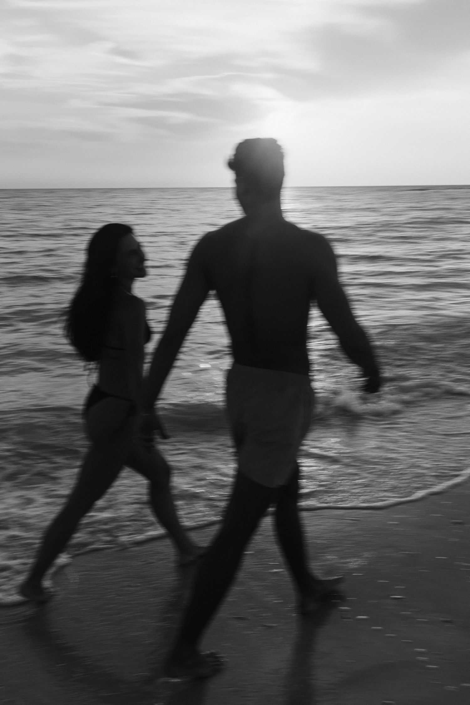 Silhouettes of two people dancing playfully along a beach at sunset.