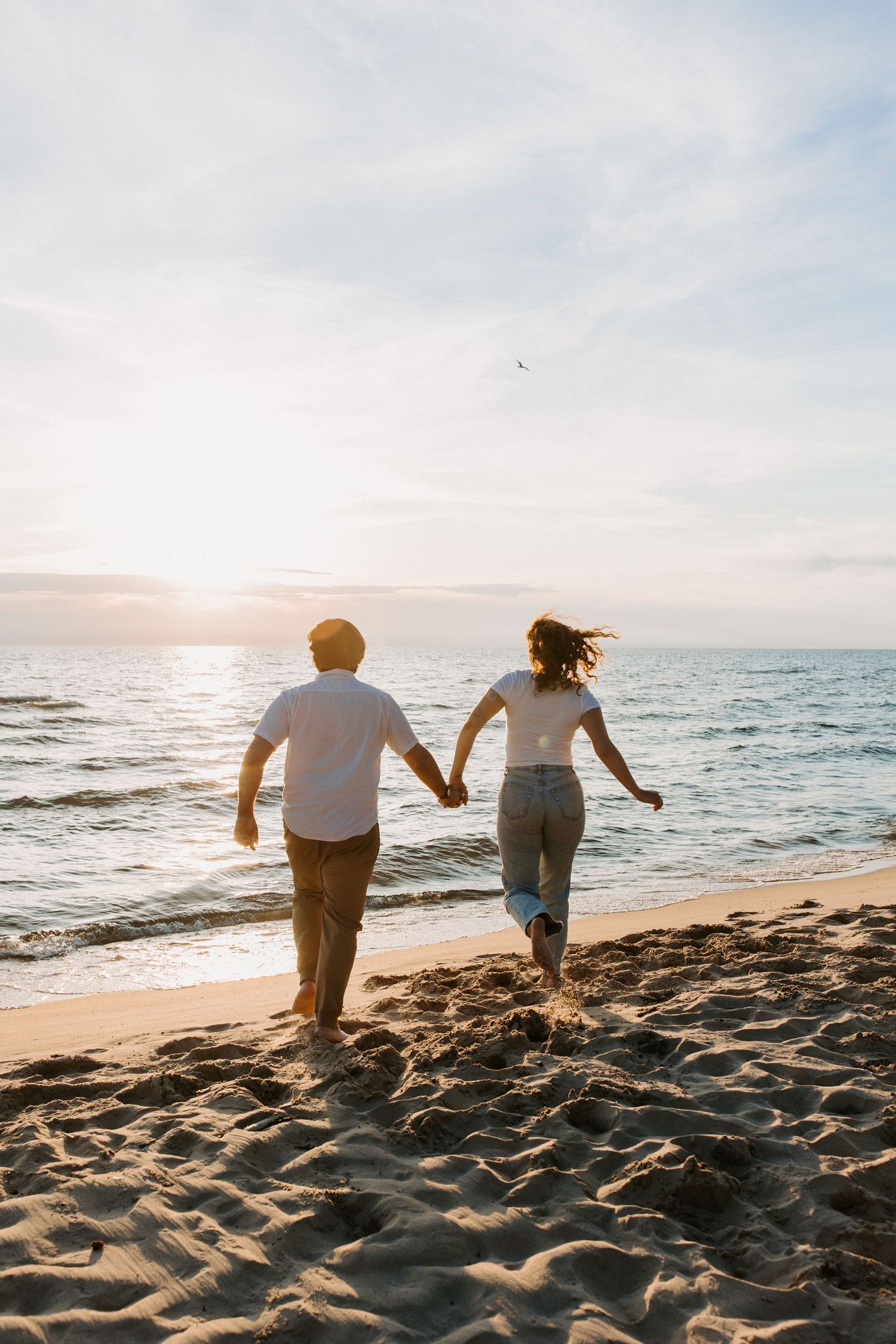 Two people running together on a sandy beach at sunset.