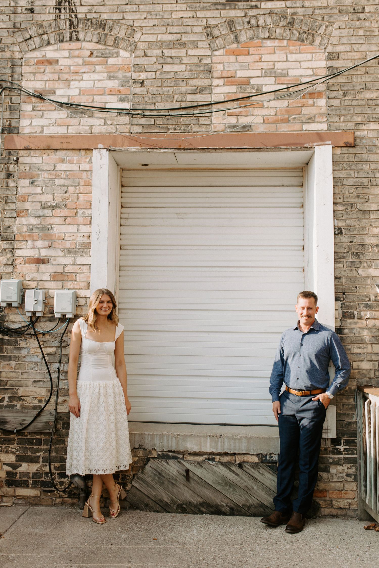 Playful engagement photo sequence against a rustic brick wall with white garage door.