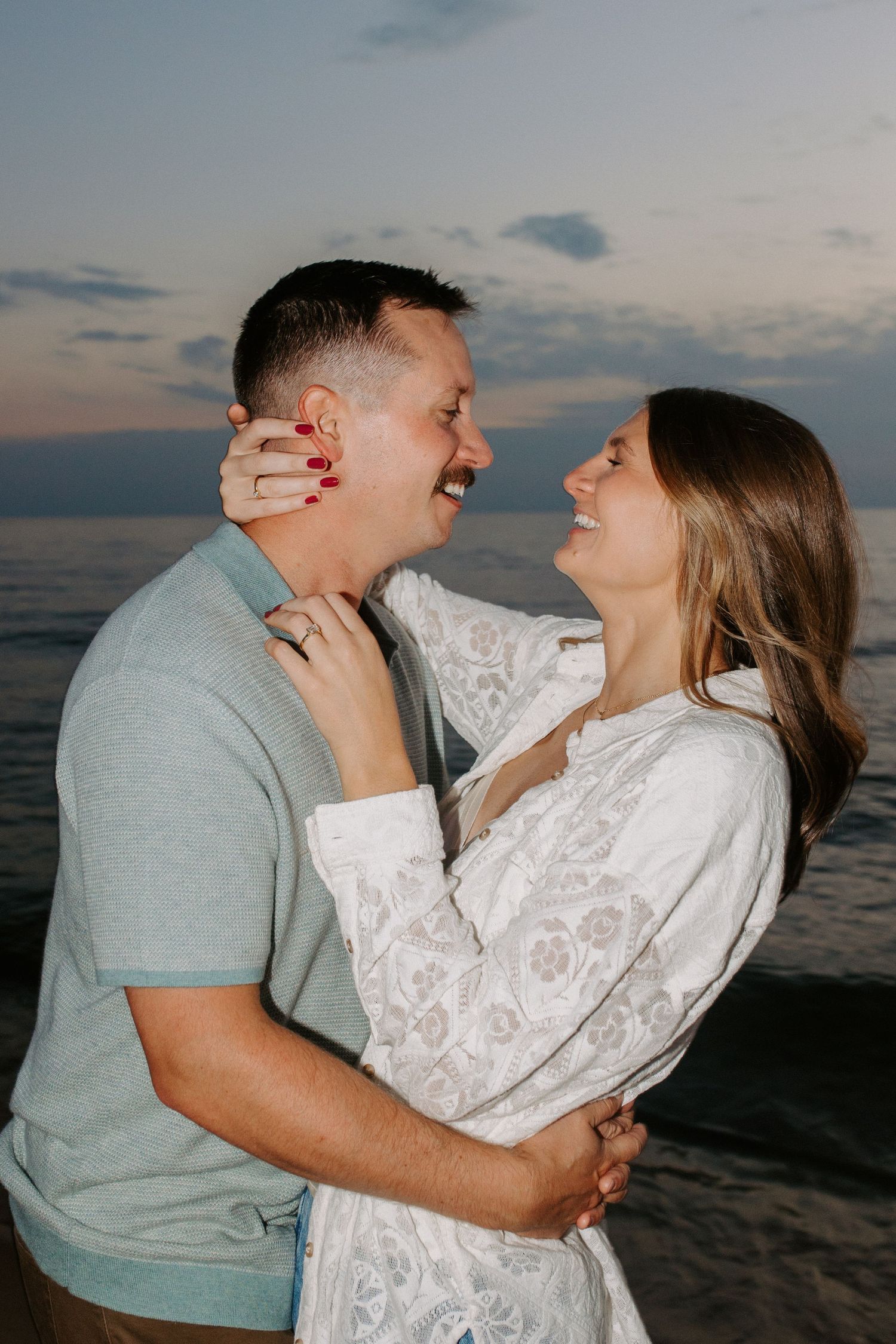A couple sharing laughter and embraces on the beach during sunset.