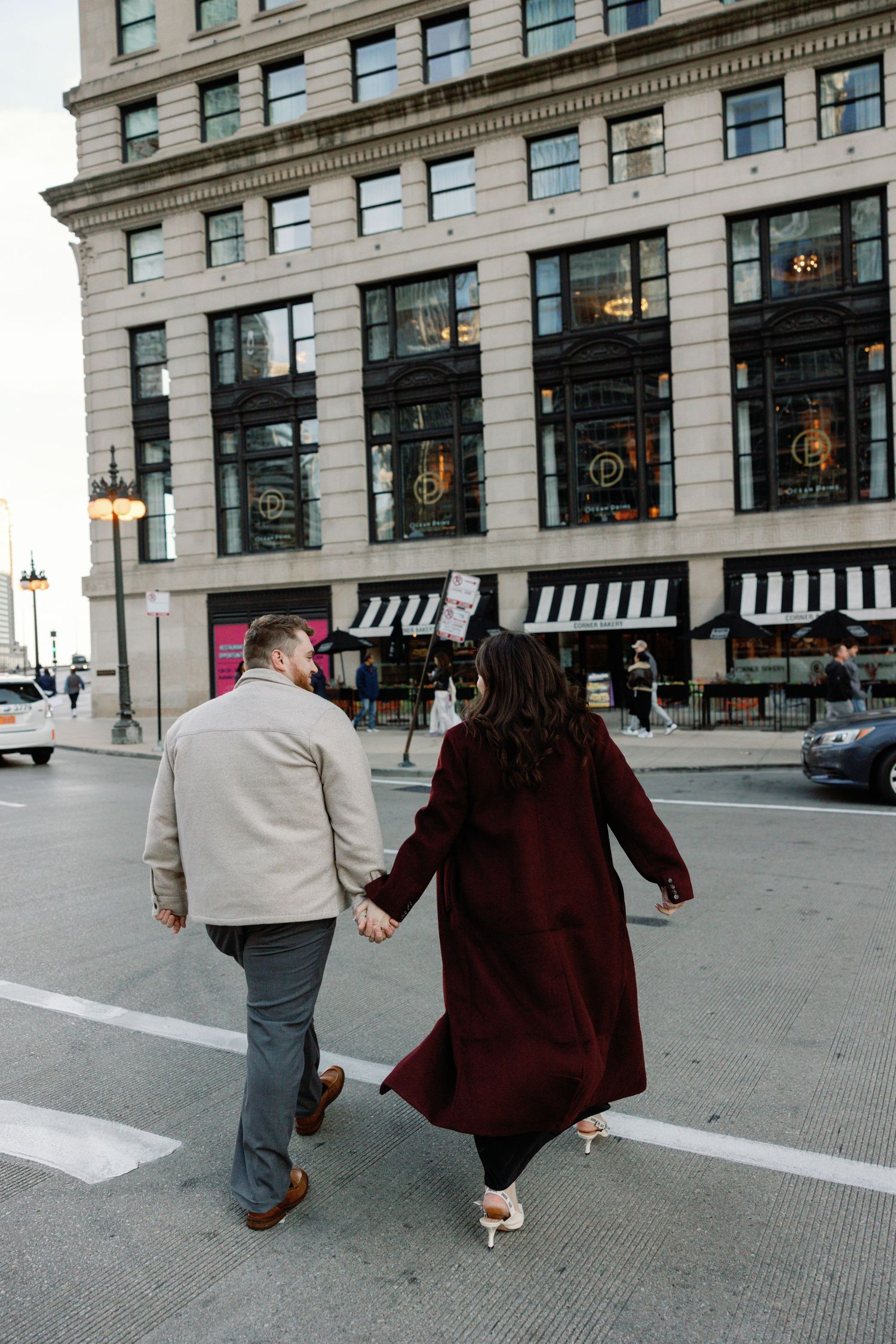 Couple walking hand in hand down a city sidewalk in front of a historic building.