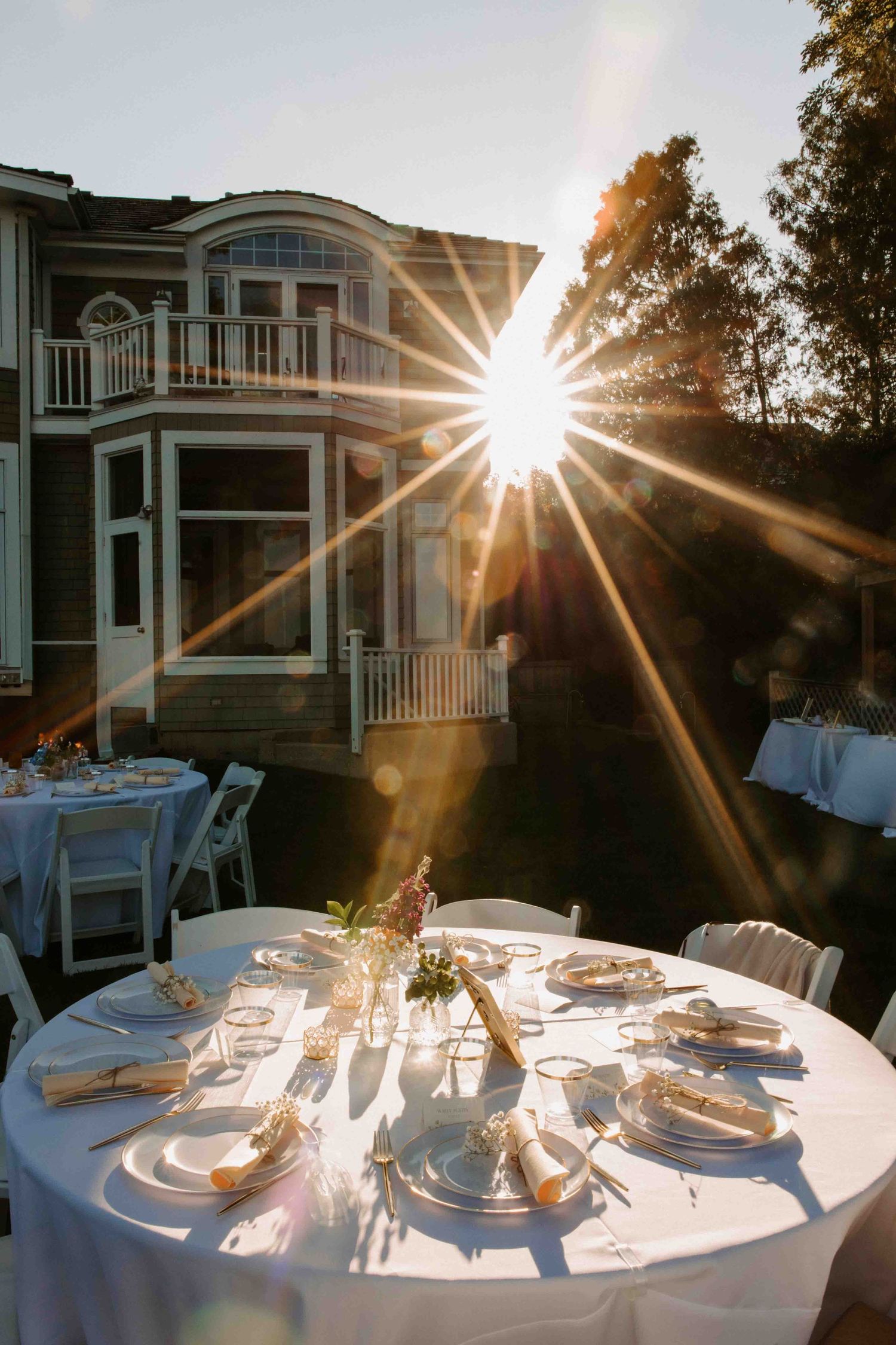 Sunlit wedding reception tables set up outdoors with elegant place settings.
