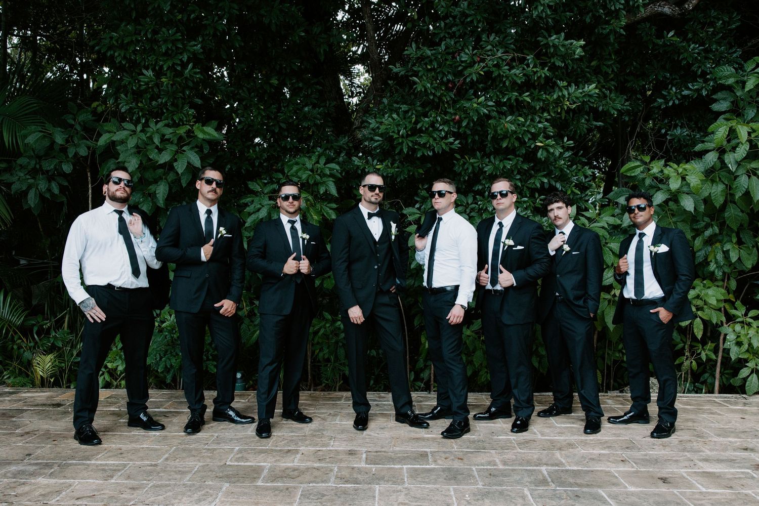 Wedding party performing synchronized jump shot outdoors in formal attire.
