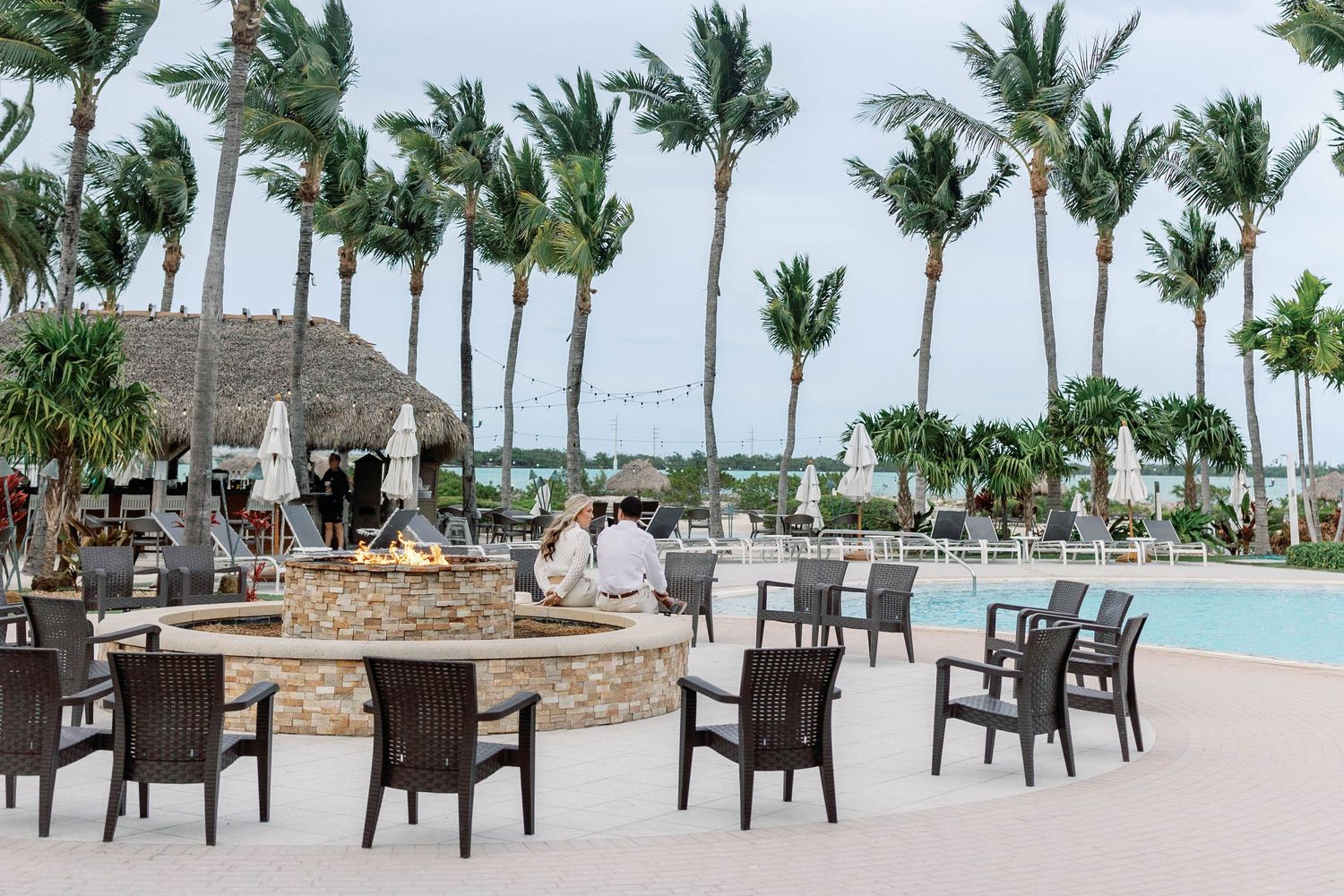 Luxurious beachfront resort with palm trees, pool, and outdoor seating areas overlooking the tropical coastline.