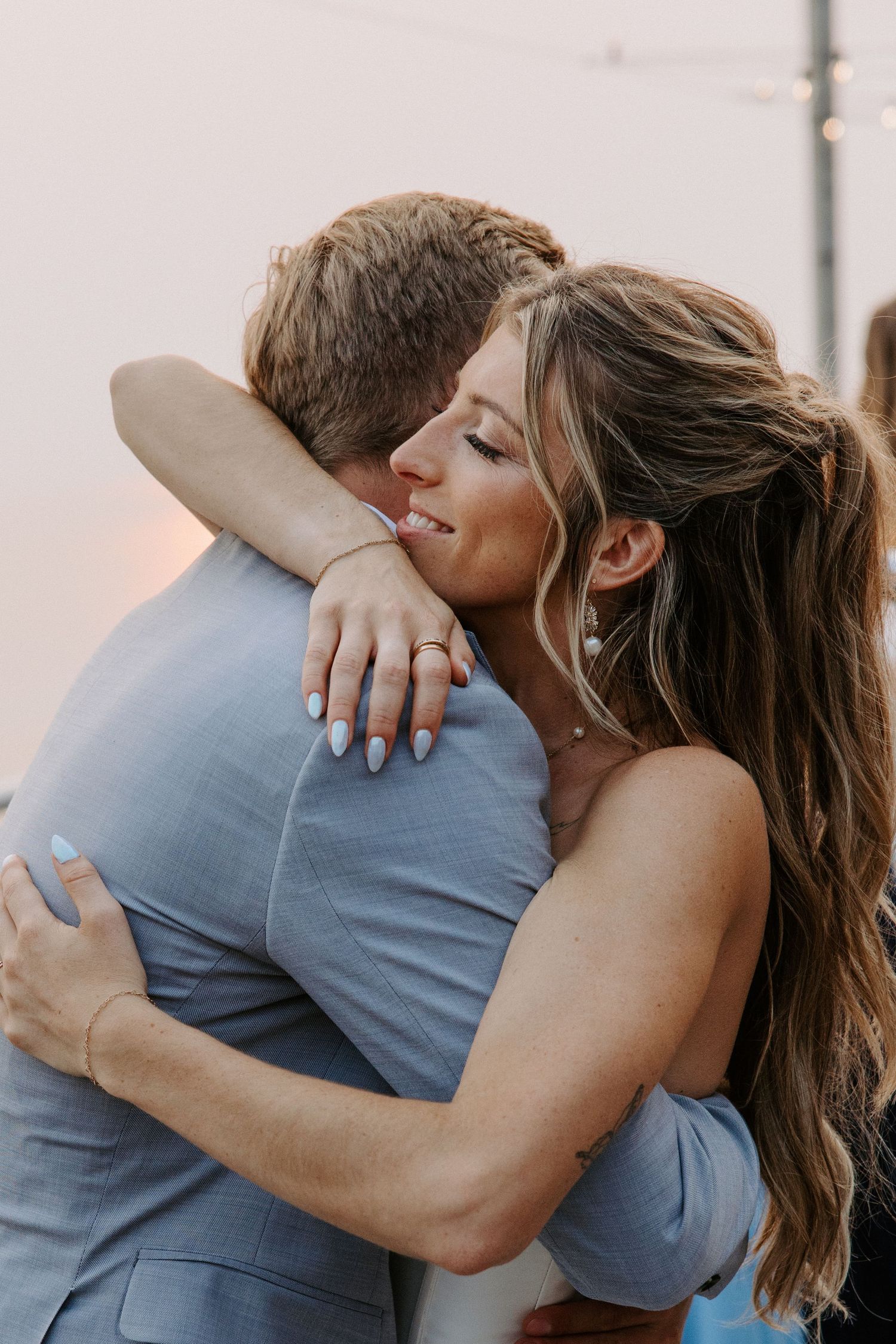 Romantic couple embraces on a boardwalk during sunset, with the bride wearing a white dress and groom in light blue suit.