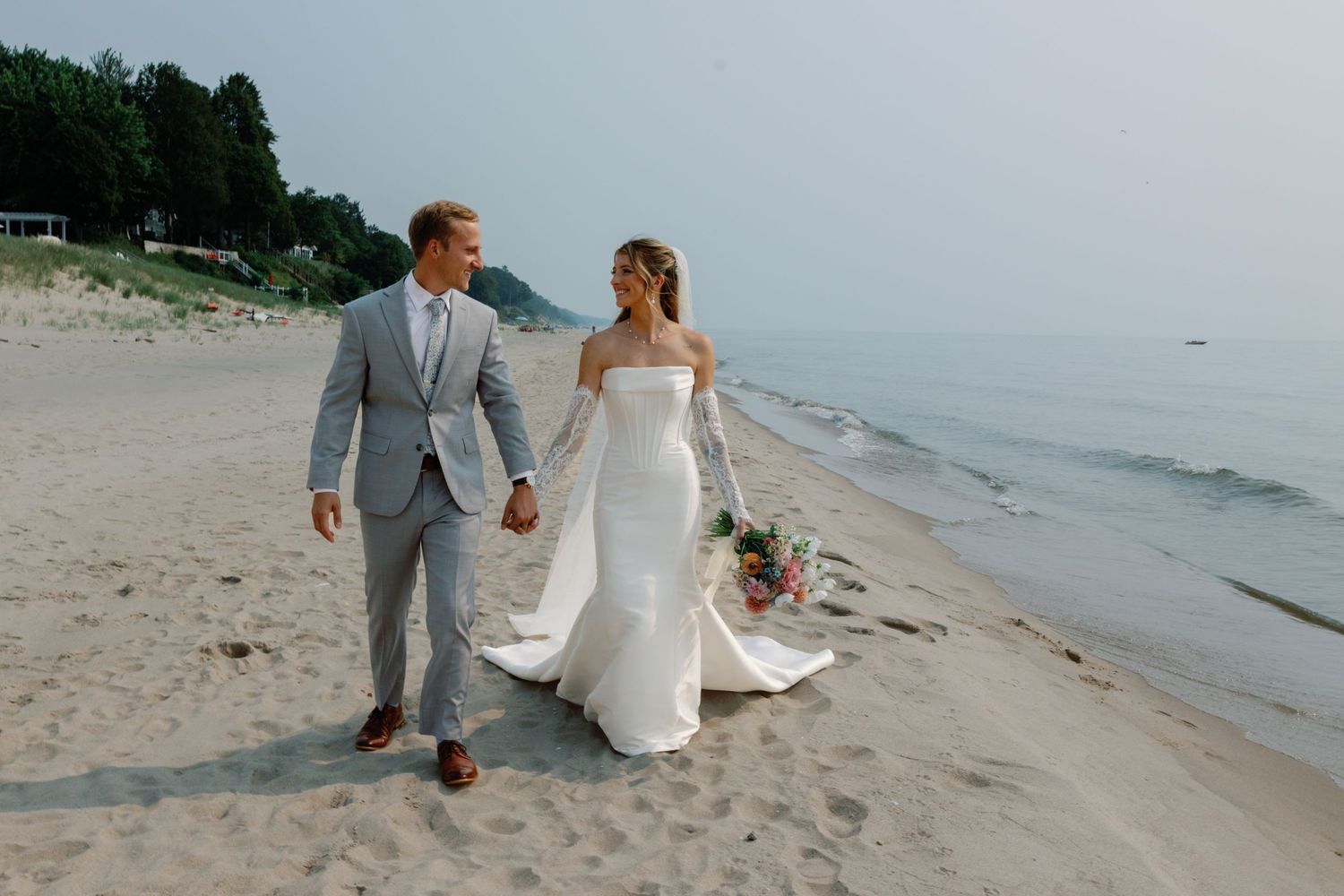 Romantic beach wedding portraits of couple walking along shoreline in formal attire.