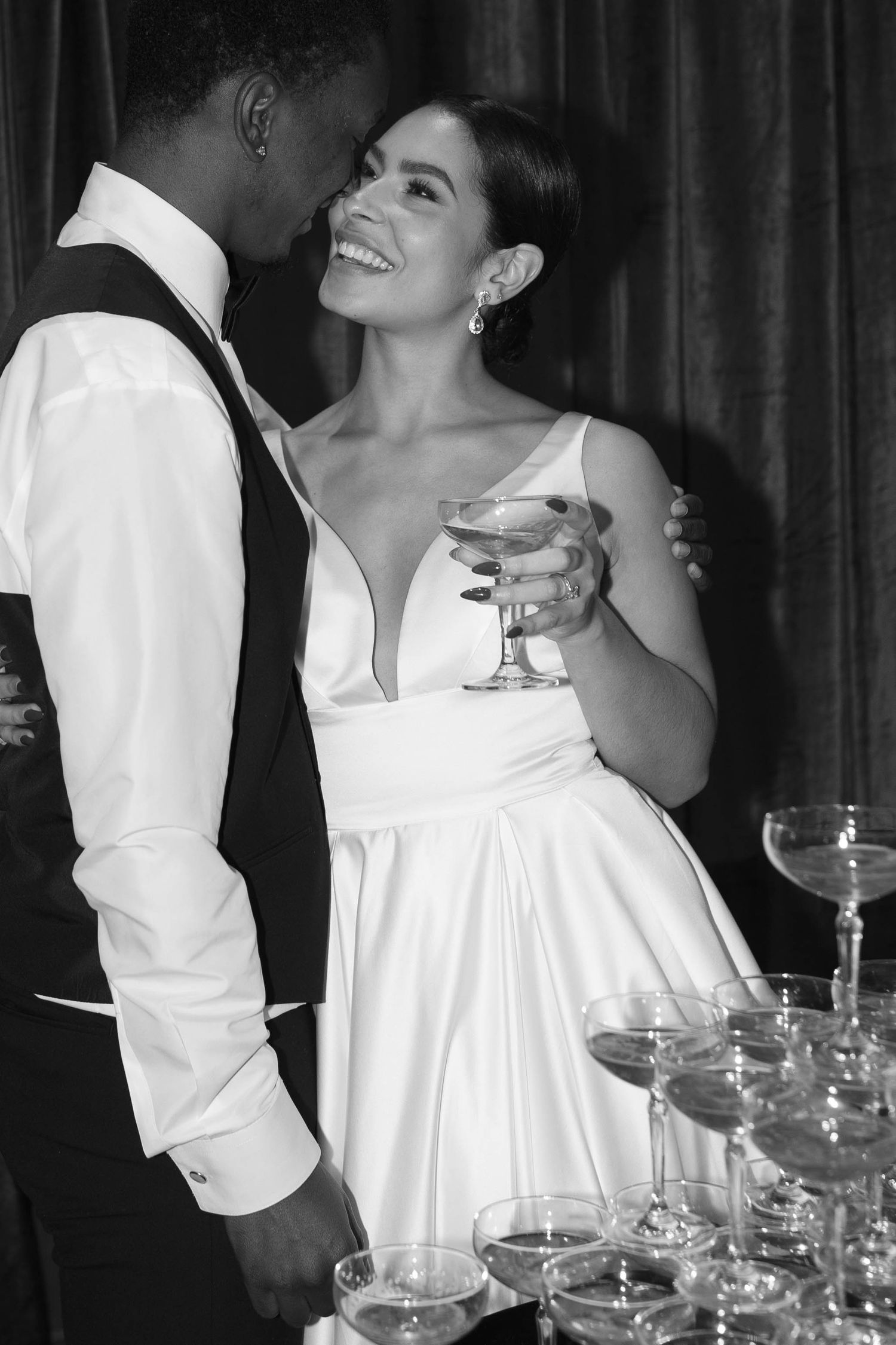 Candid black and white photo of a couple laughing near champagne glasses at their wedding.