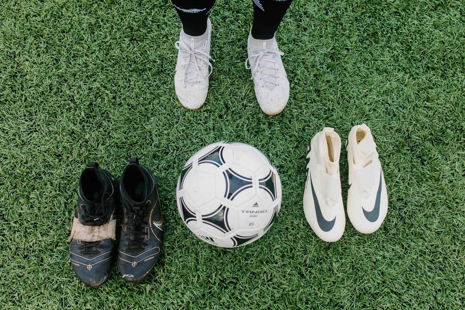 Collection of soccer cleats and balls arranged on green turf field.