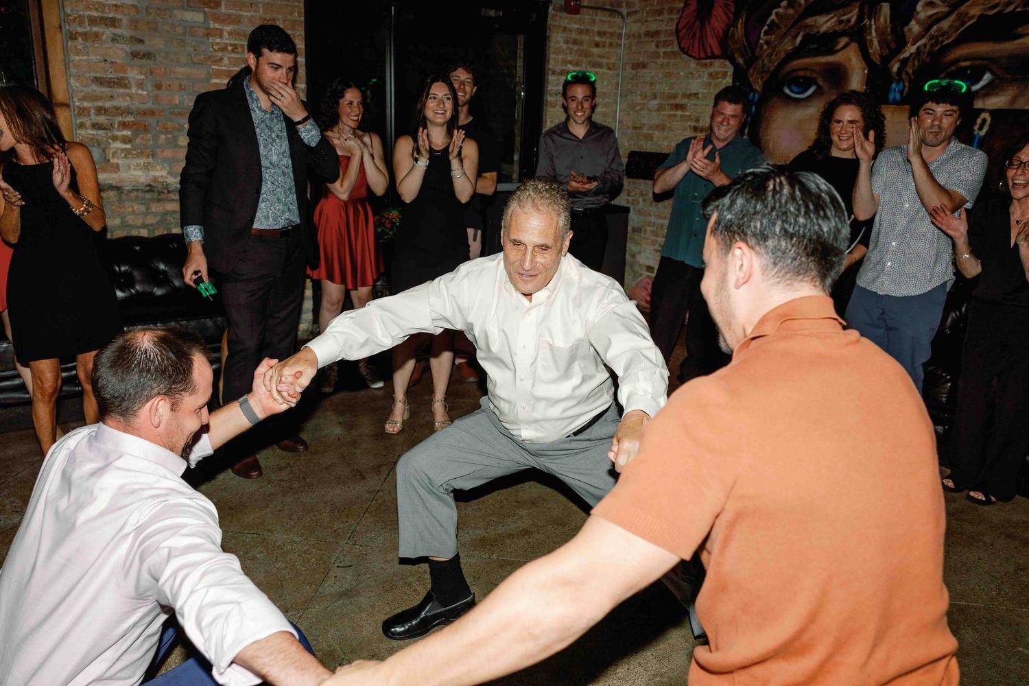 People dancing and celebrating at a lively indoor party with brick wall backdrop.