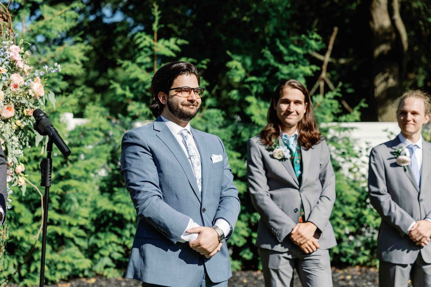 Wedding party in coordinated gray attire poses outdoors against lush greenery.