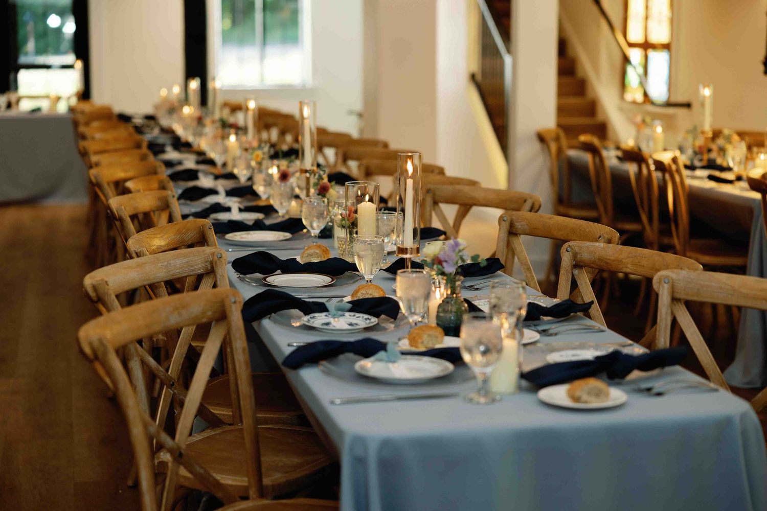Wedding reception tables decorated with blue linens and place settings in a bright indoor venue.