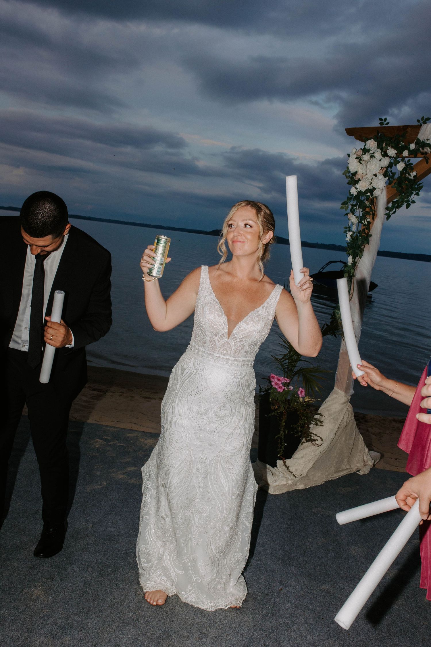 A bride in white dress kneeling on ground holding glowing light tubes during nighttime celebration.