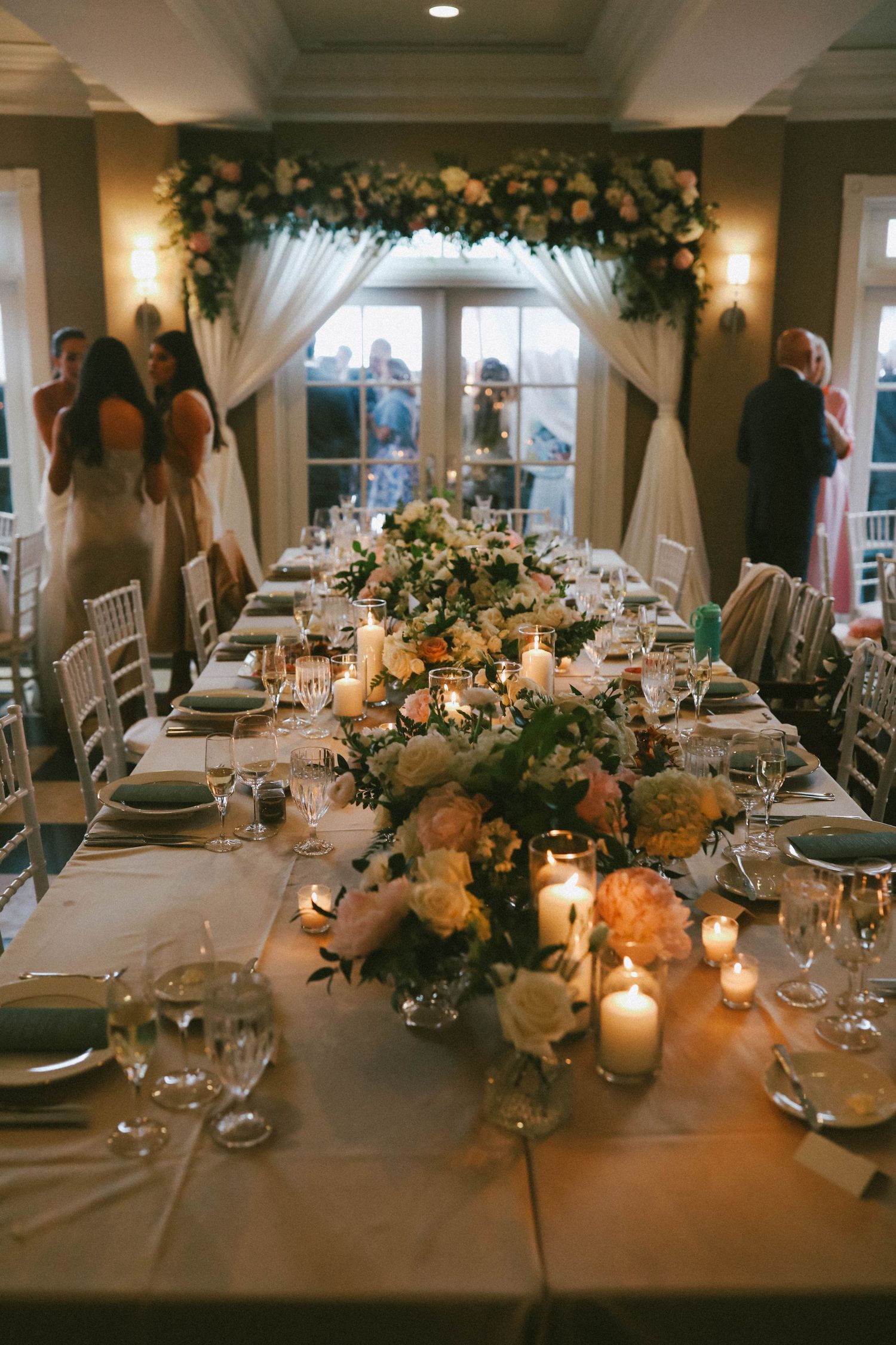 Wedding reception dining room with elegant table settings, floral arrangements and soft lighting.