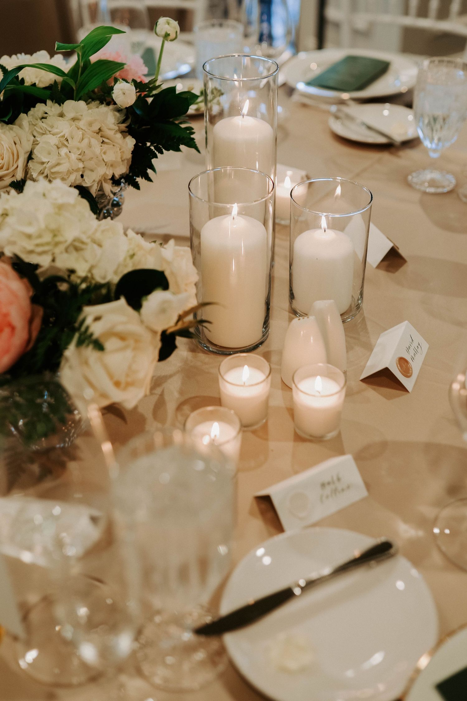 Elegant wedding reception table setting with white flowers and glowing candles in glass holders.