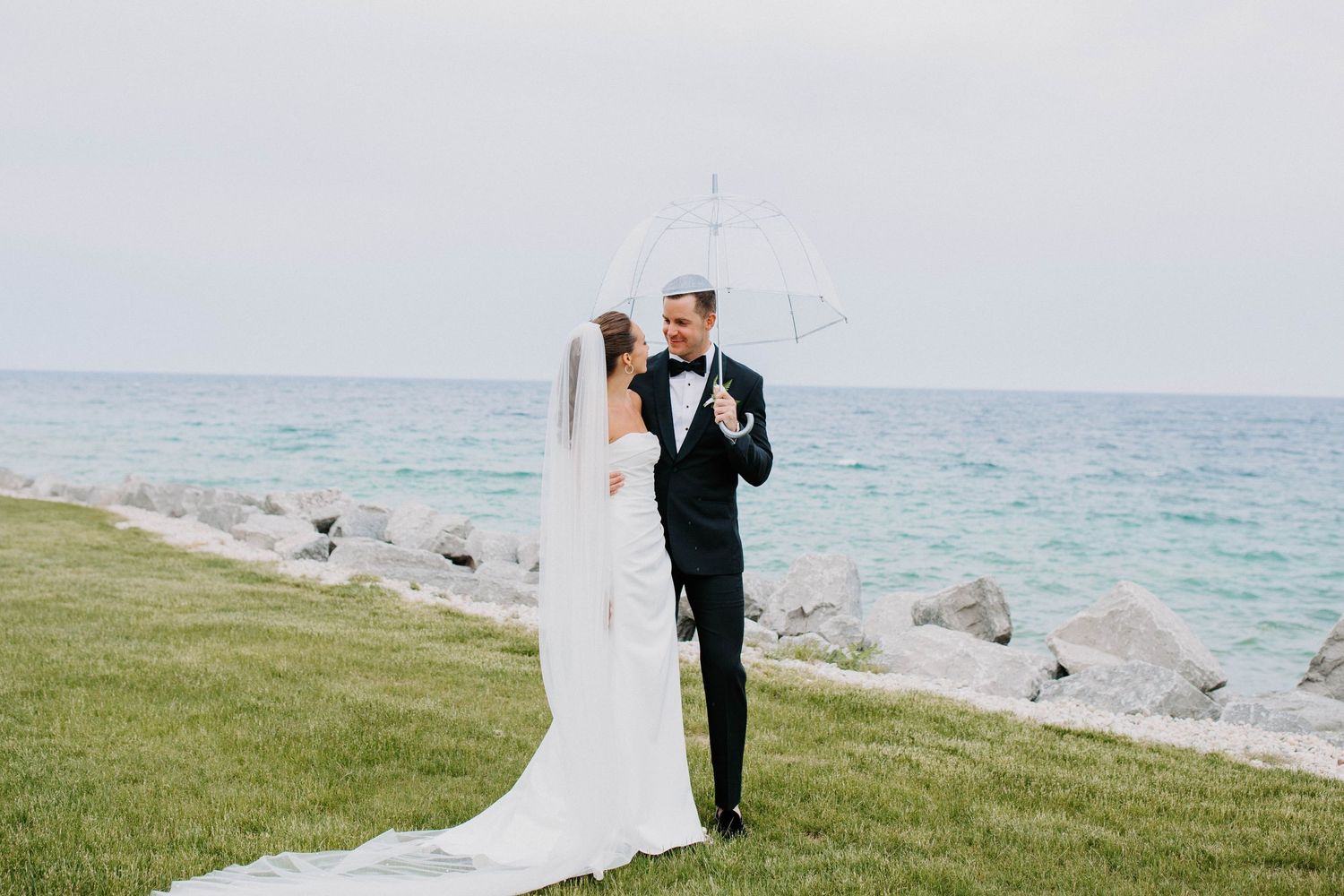 Newlyweds standing on grassy oceanfront during their wedding celebration.