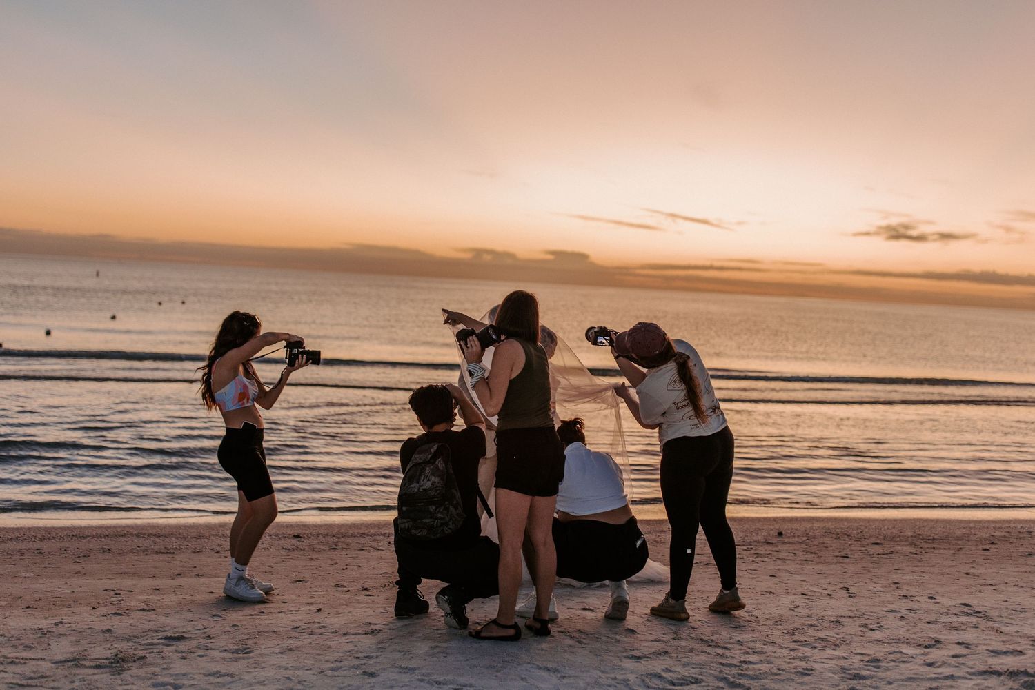 A series of silhouetted figures playing and enjoying activities on a beach at sunset with golden sky and ocean backdrop.