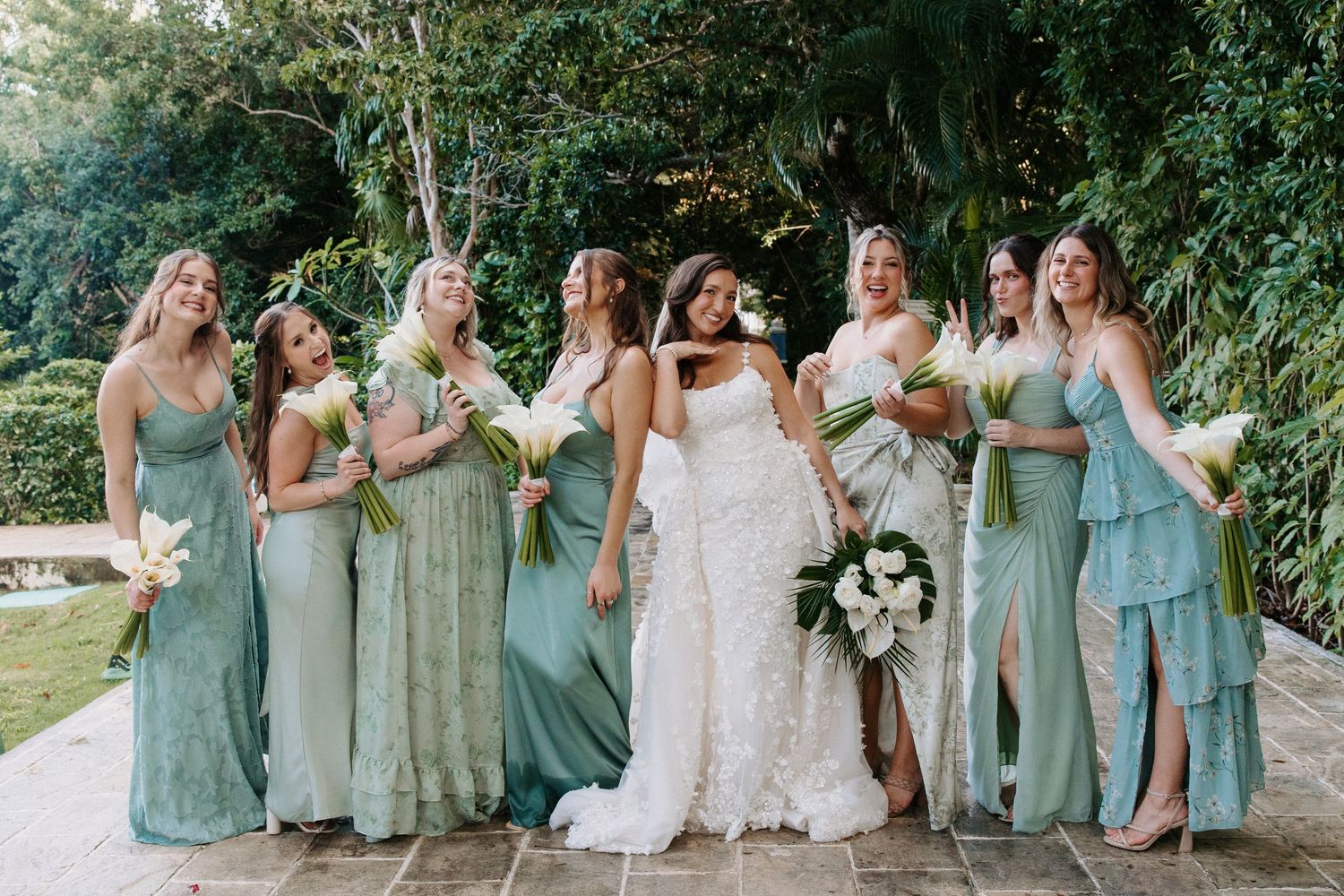 Bridesmaids in mint green dresses laughing and celebrating with bride outdoors.