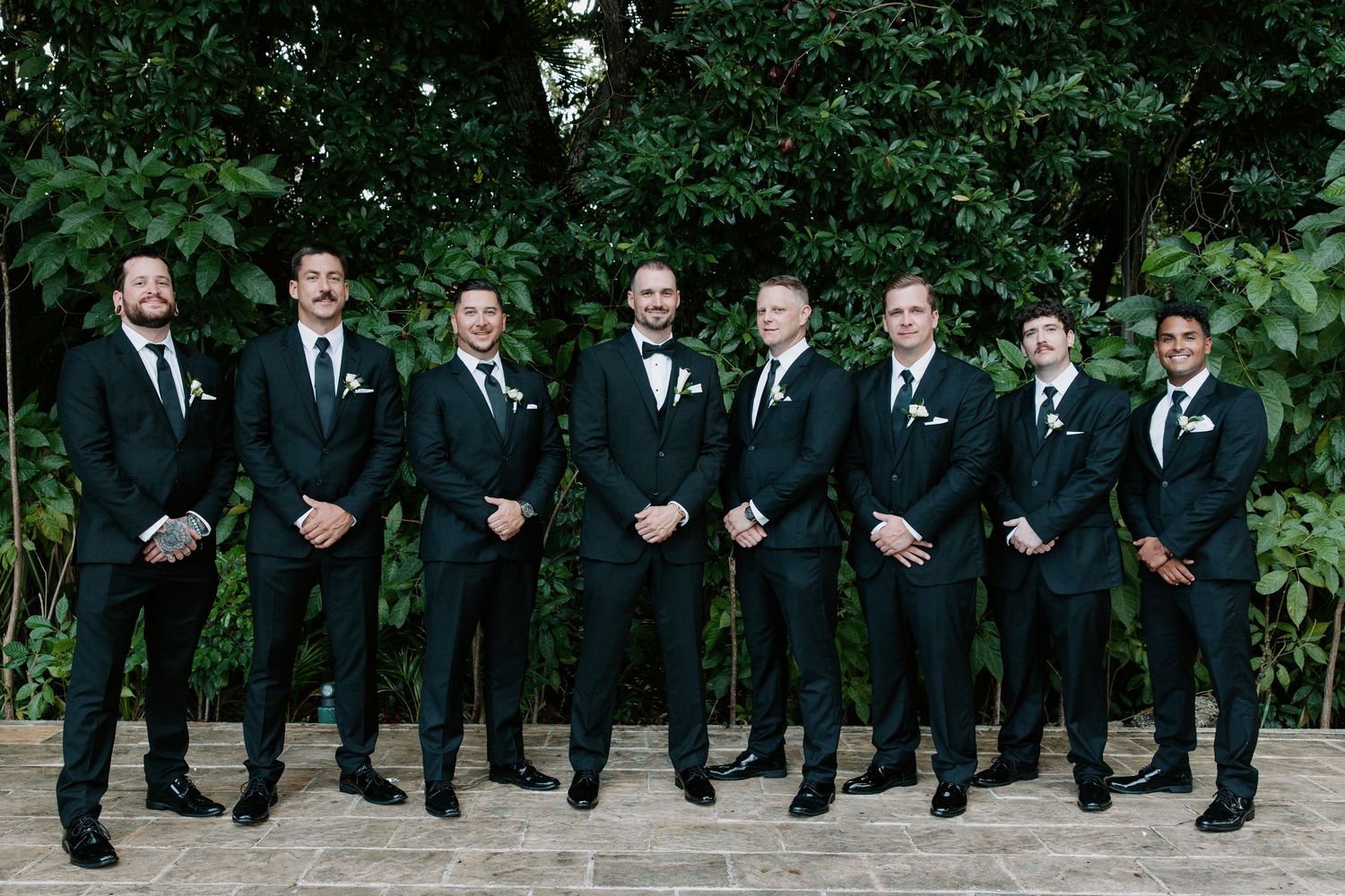 Wedding party members in formal black suits posing together outdoors.