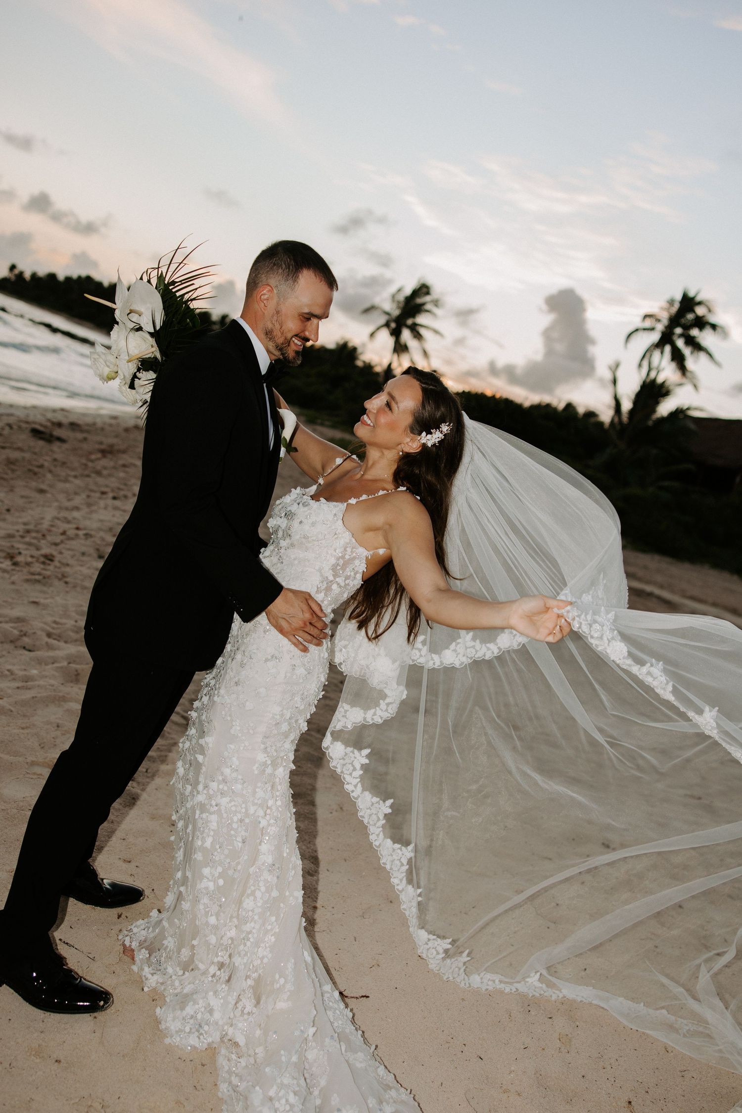 A romantic beach wedding photoshoot featuring a flowing white dress and veil against a sunset backdrop.
