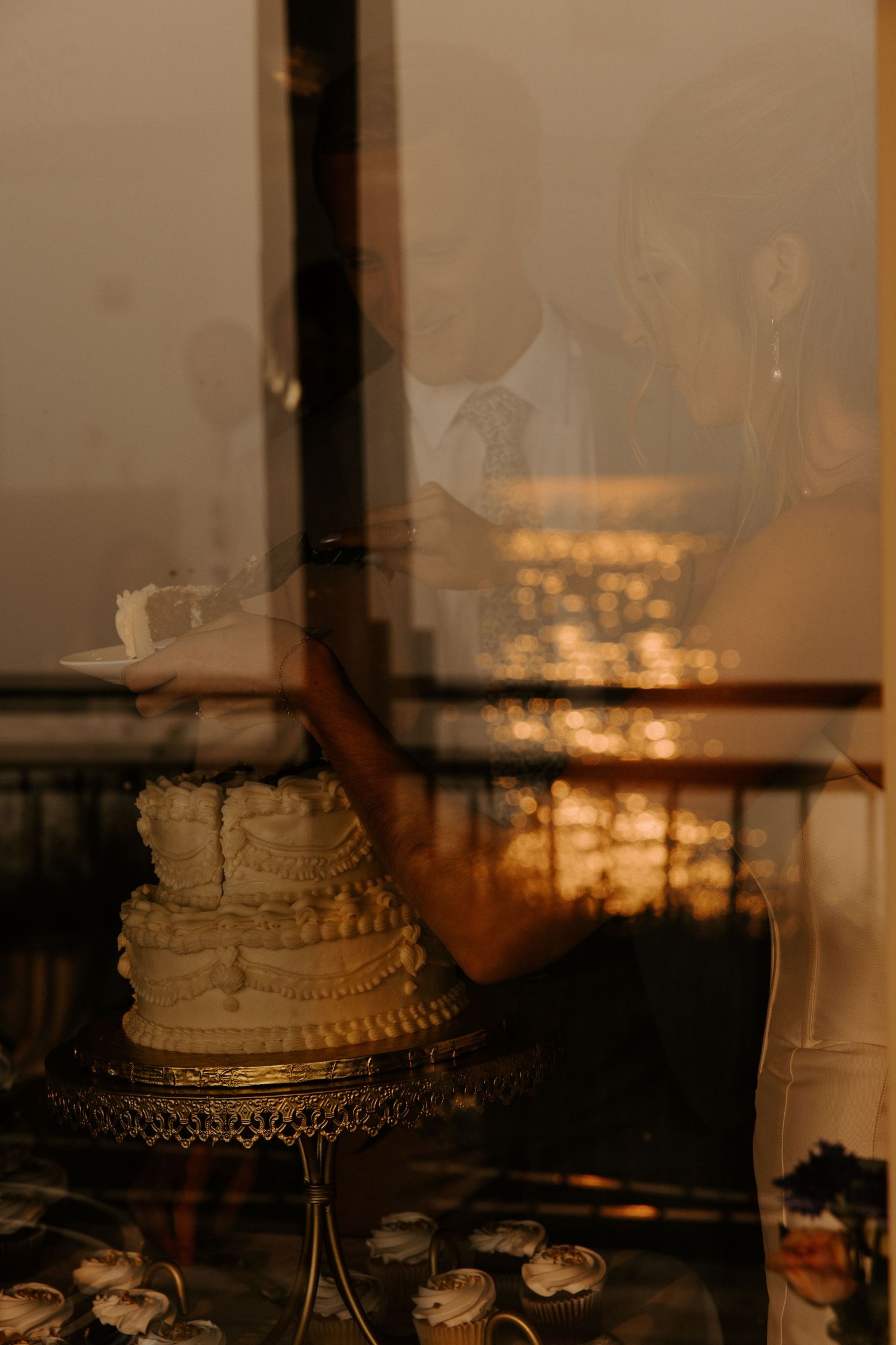 Wedding cake silhouetted against a sunset window during reception.