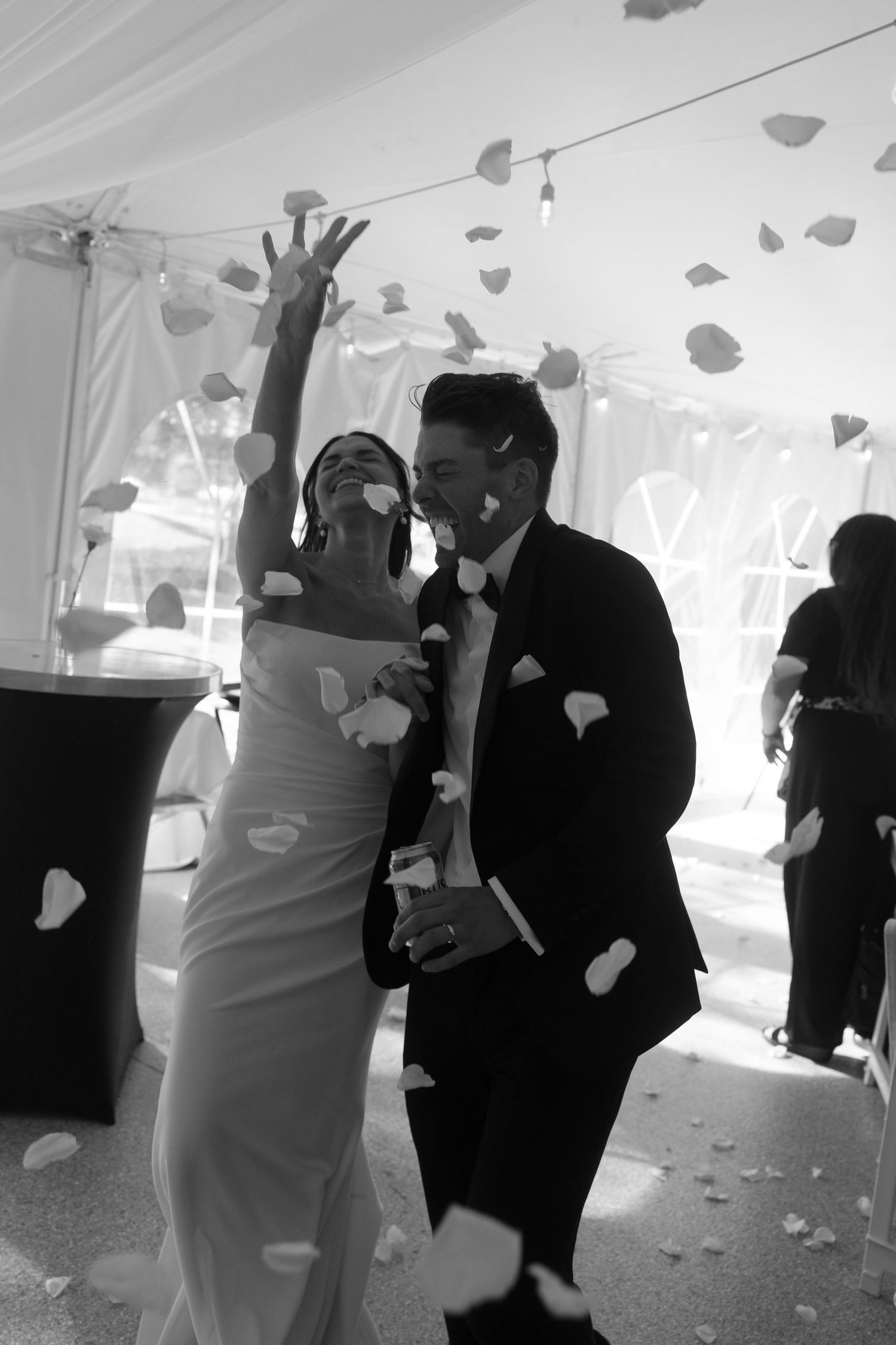 Wedding couple dances in a white tent while rose petals fall around them during their first dance.
