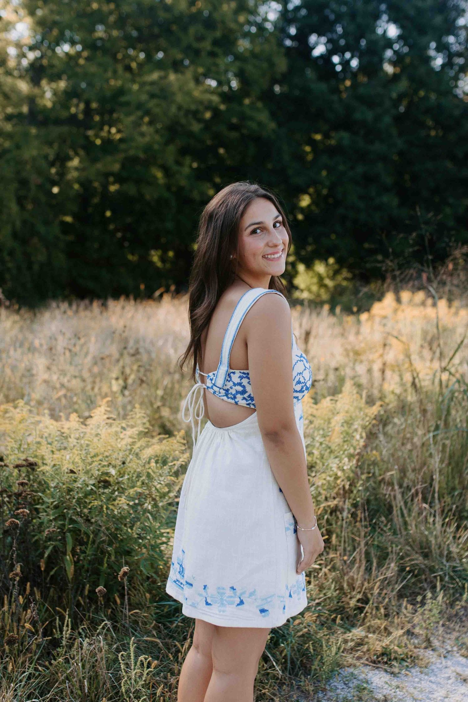 Candid summer photoshoot on a dirt path with tall grass and trees in the background.