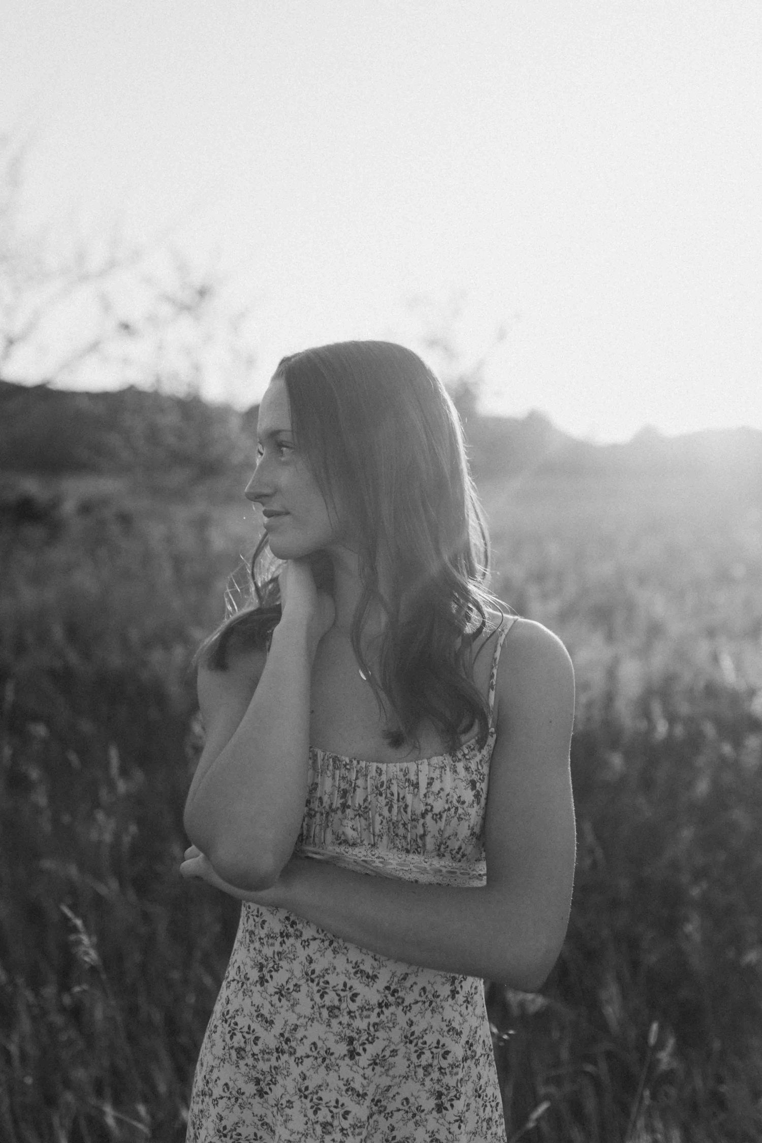 Black and white sunset portrait showing silhouetted figure in a meadow with dramatic lighting.